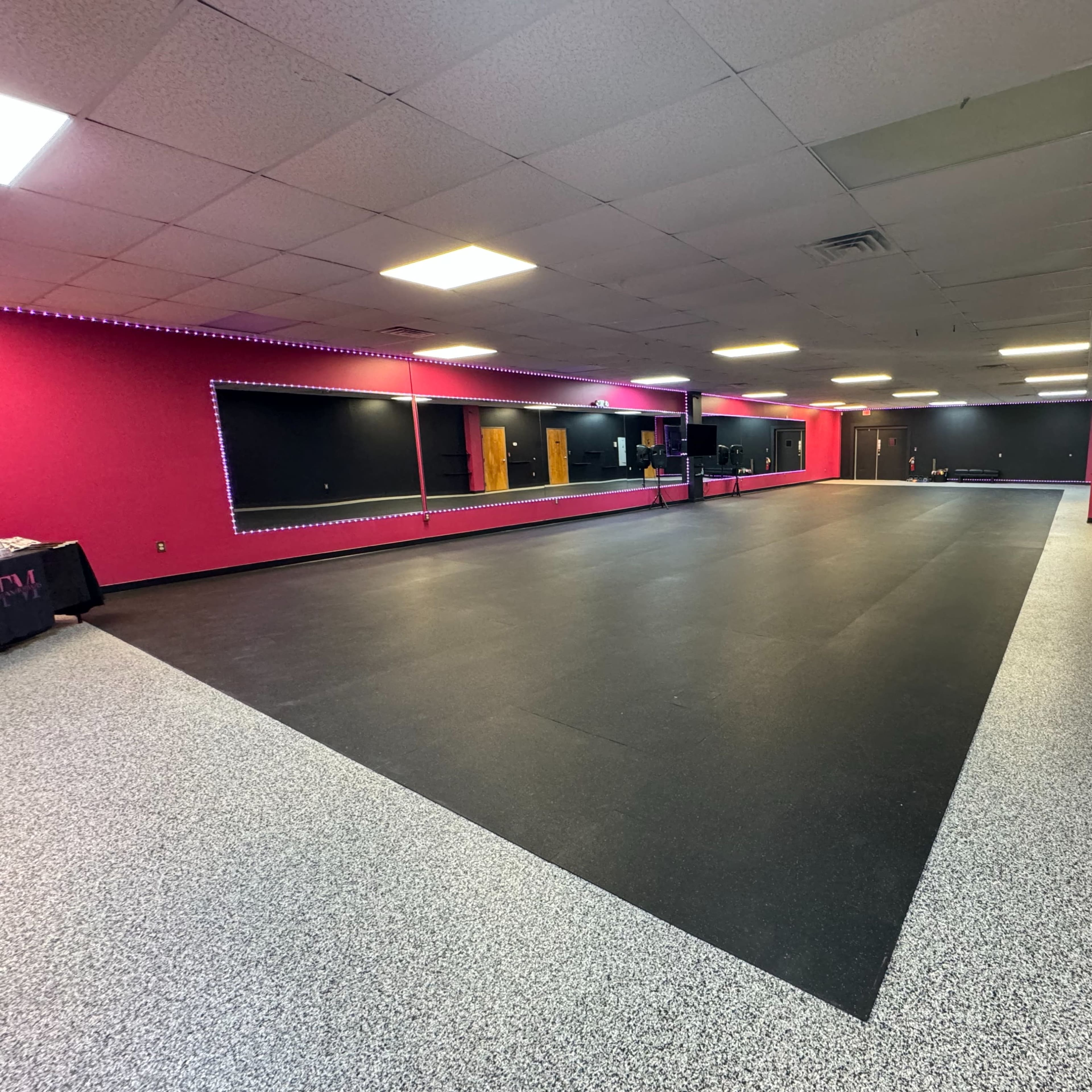 A large, empty studio space with black and pink walls and a rubberized flooring surface.