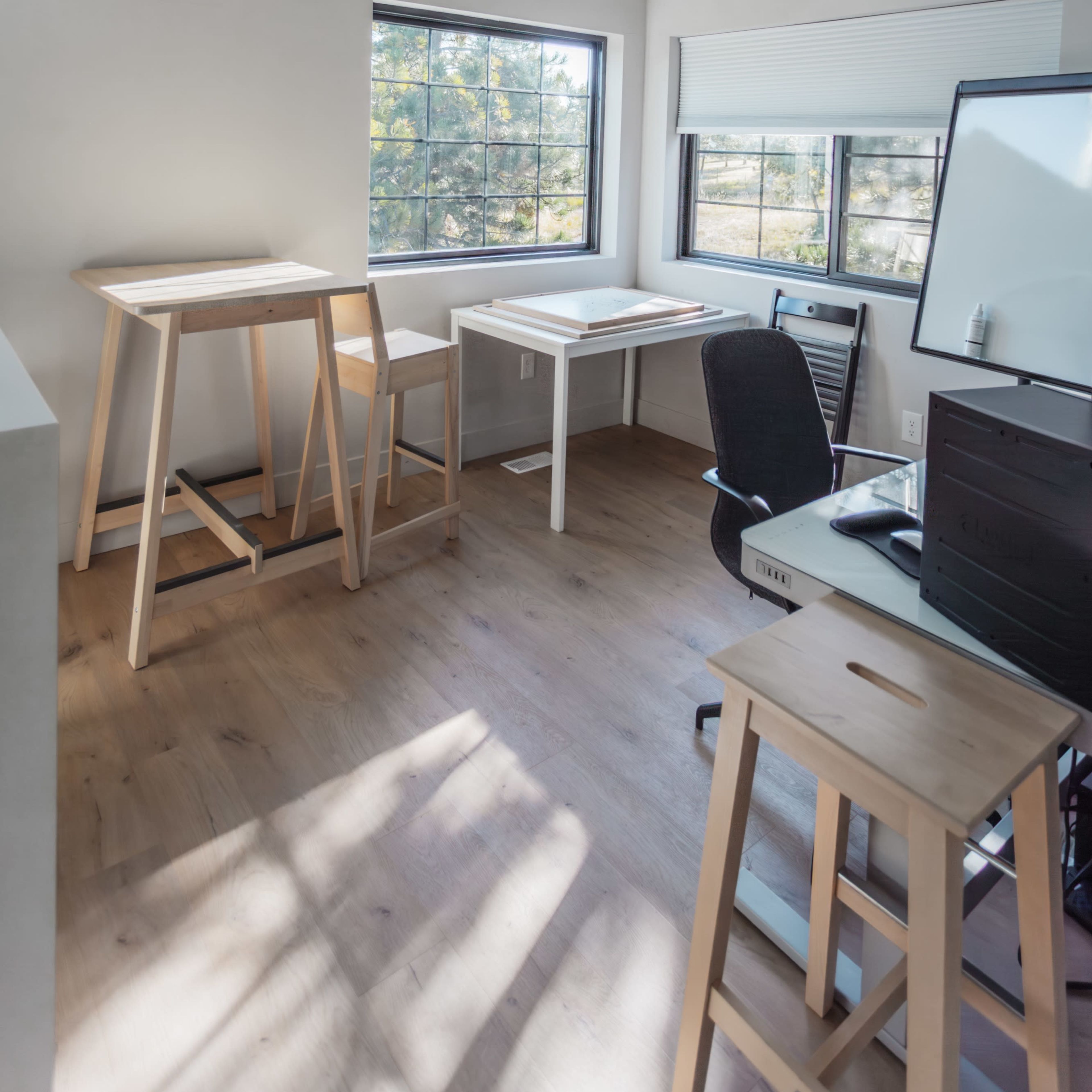 A bright office space with large windows, a standing desk, a chair, and a computer setup.