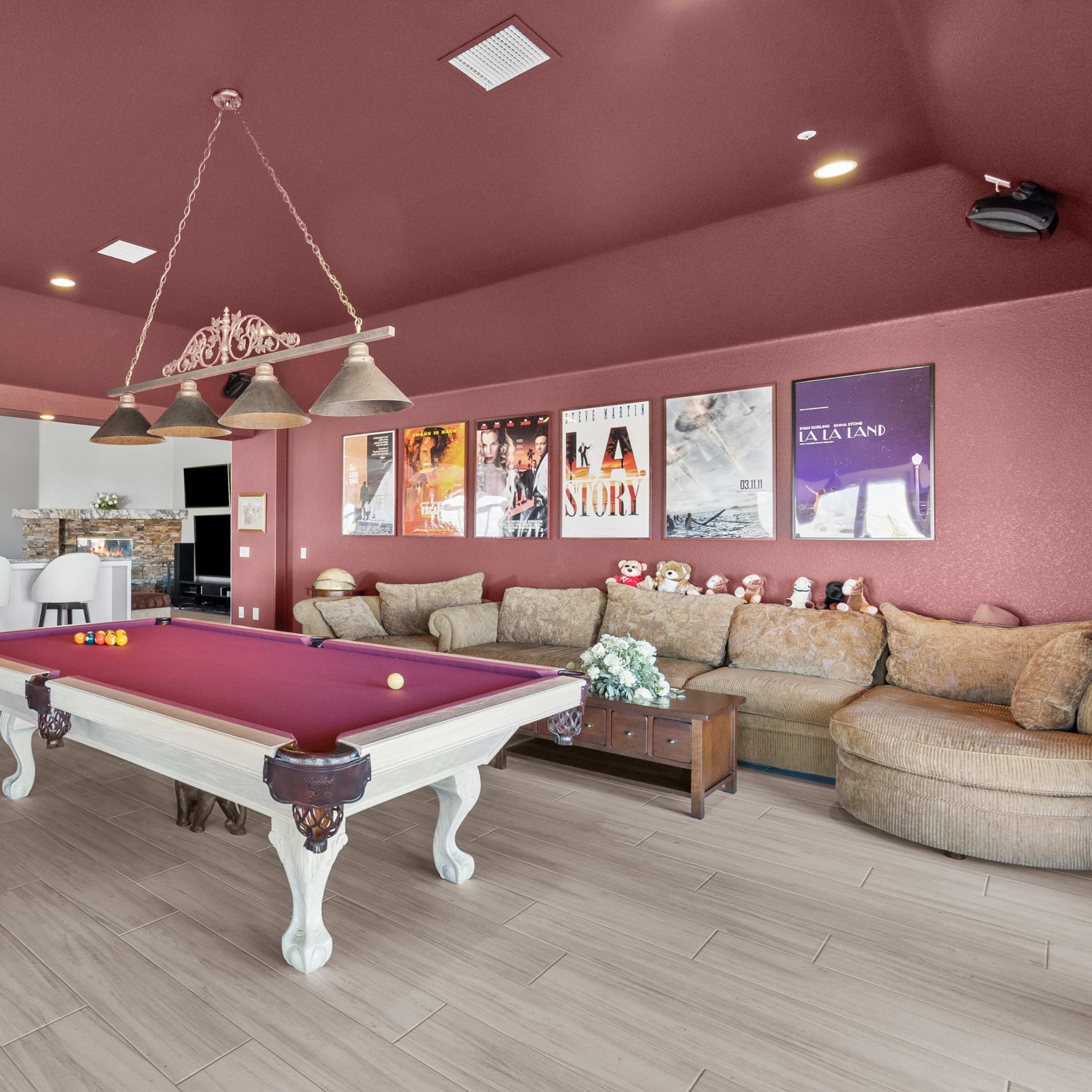 A spacious game room features a billiard table, a large sectional sofa, and movie posters on the walls.