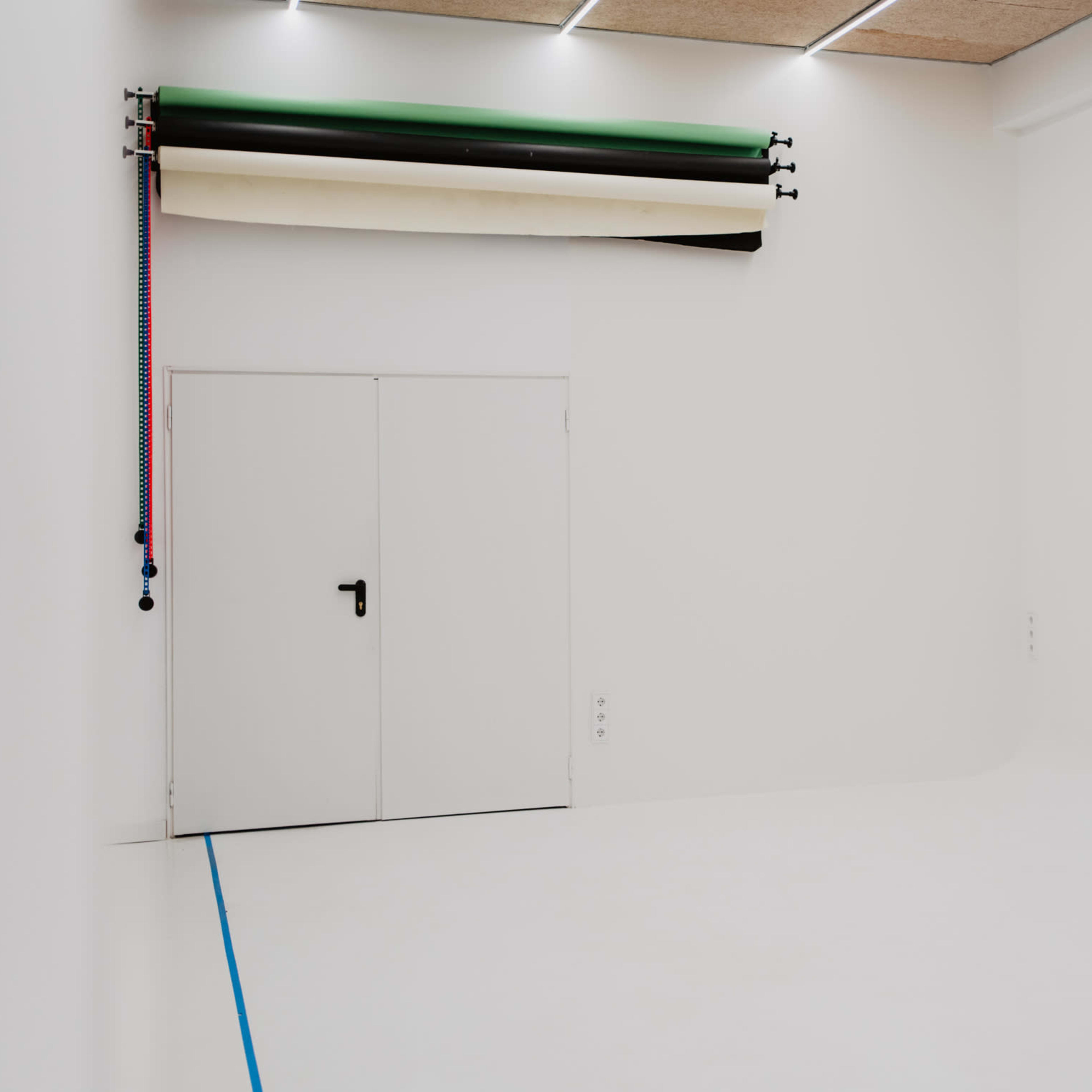 A minimalist studio space with white walls, a closed door, and several rolls of colored backdrop paper mounted on the wall.