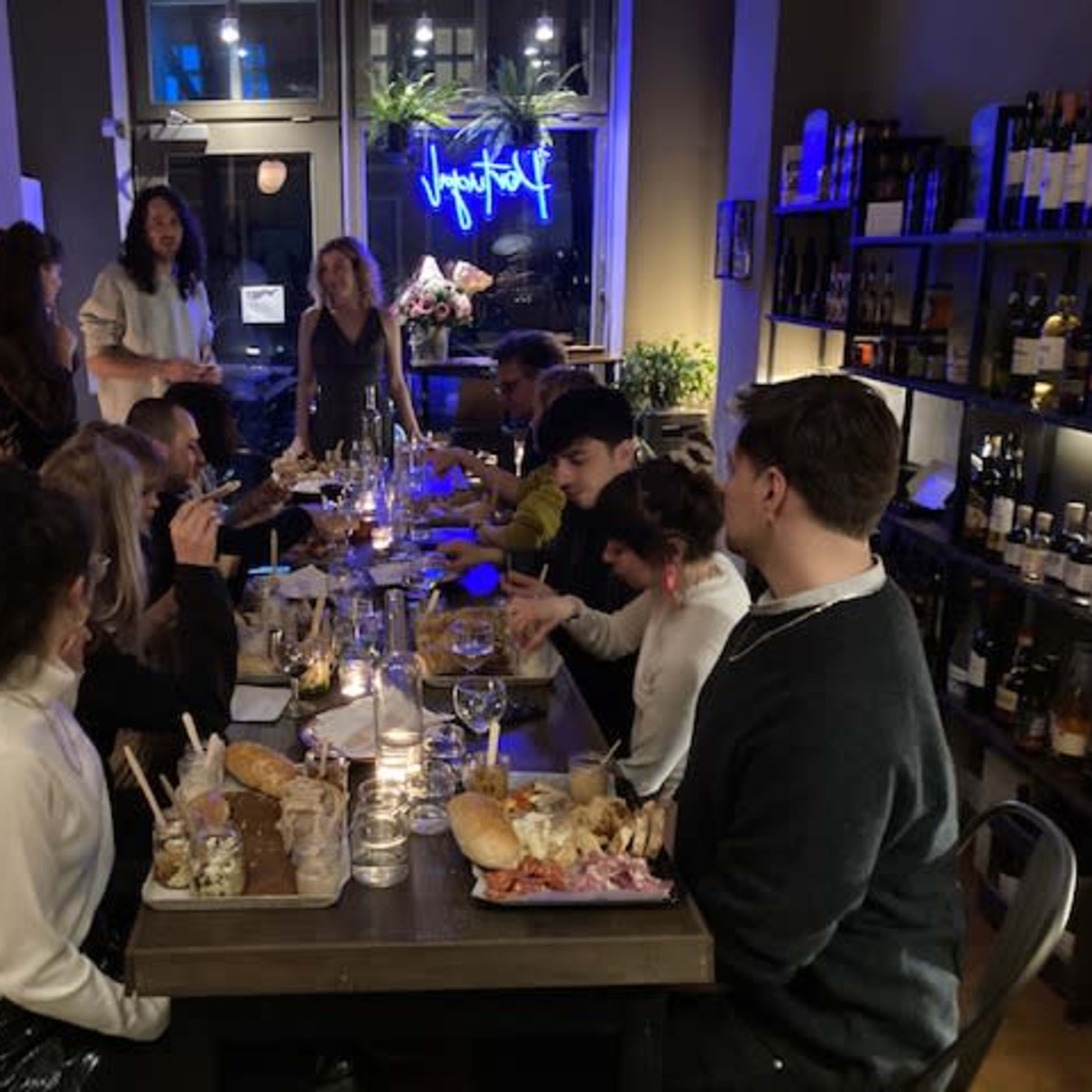 A group of people gathered around a long table filled with food and drinks in a dimly lit restaurant.