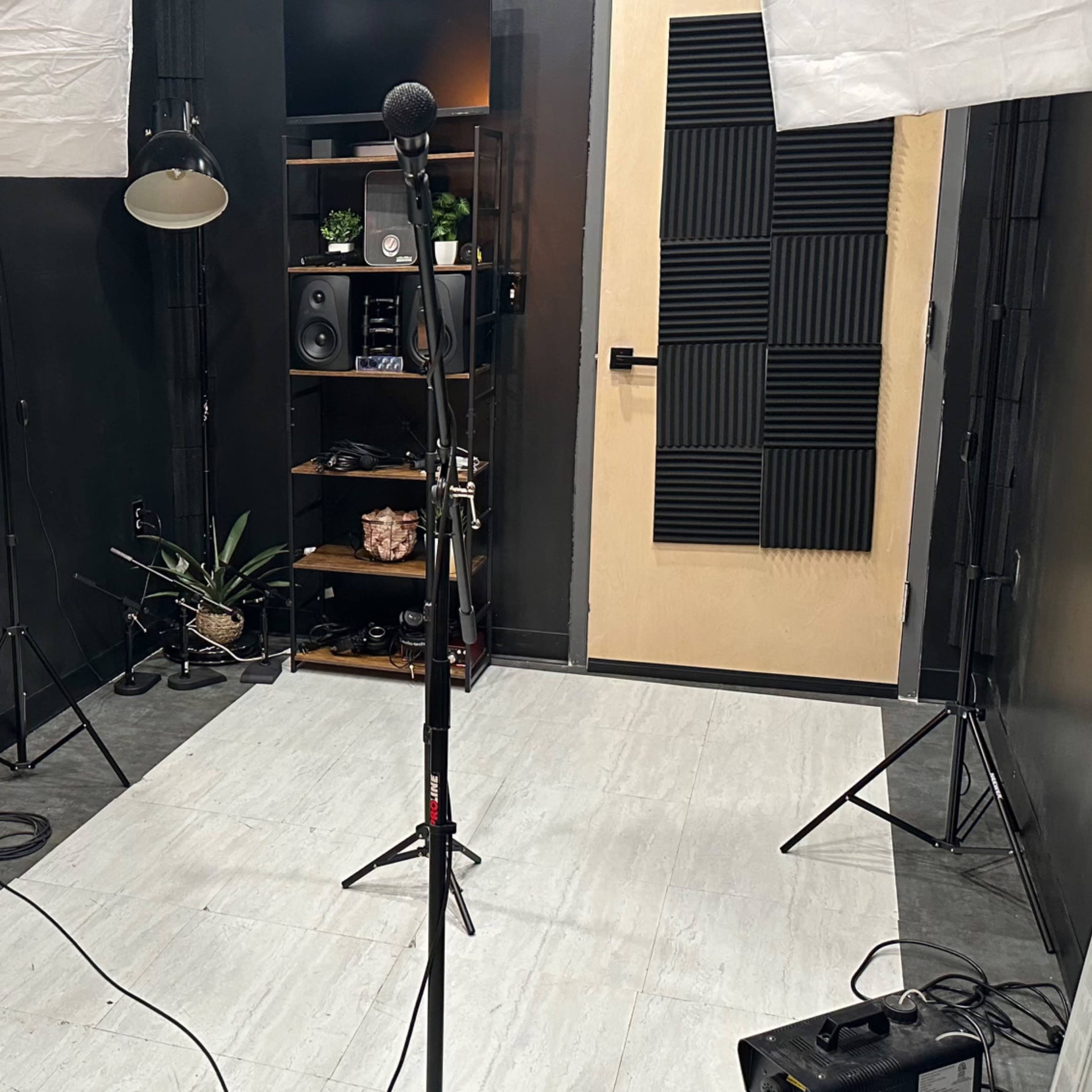 A music recording studio with a microphone stand, keyboard, and softbox lights set up against a dark wall.