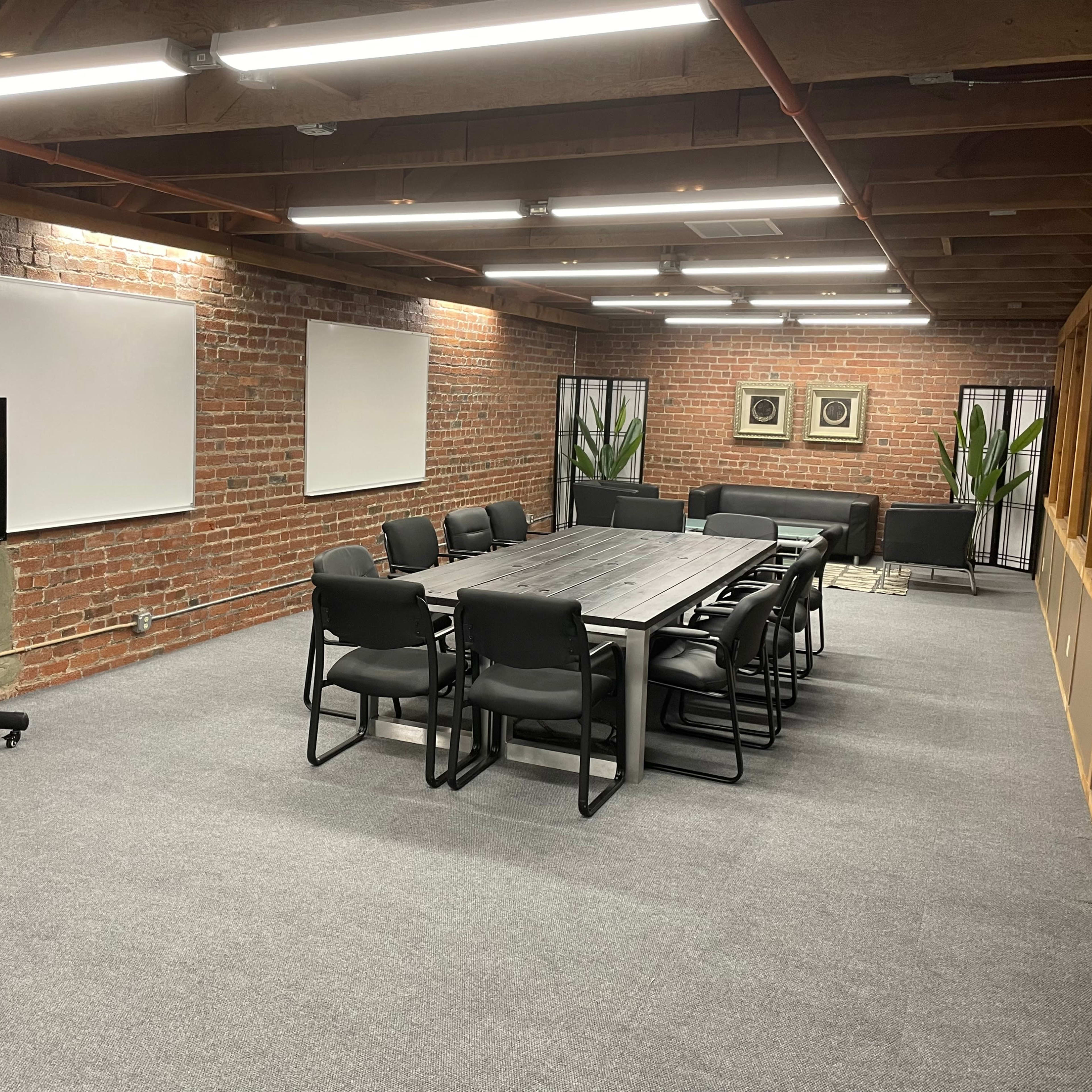 A modern conference room featuring a long table surrounded by black chairs, with brick walls and large windows.