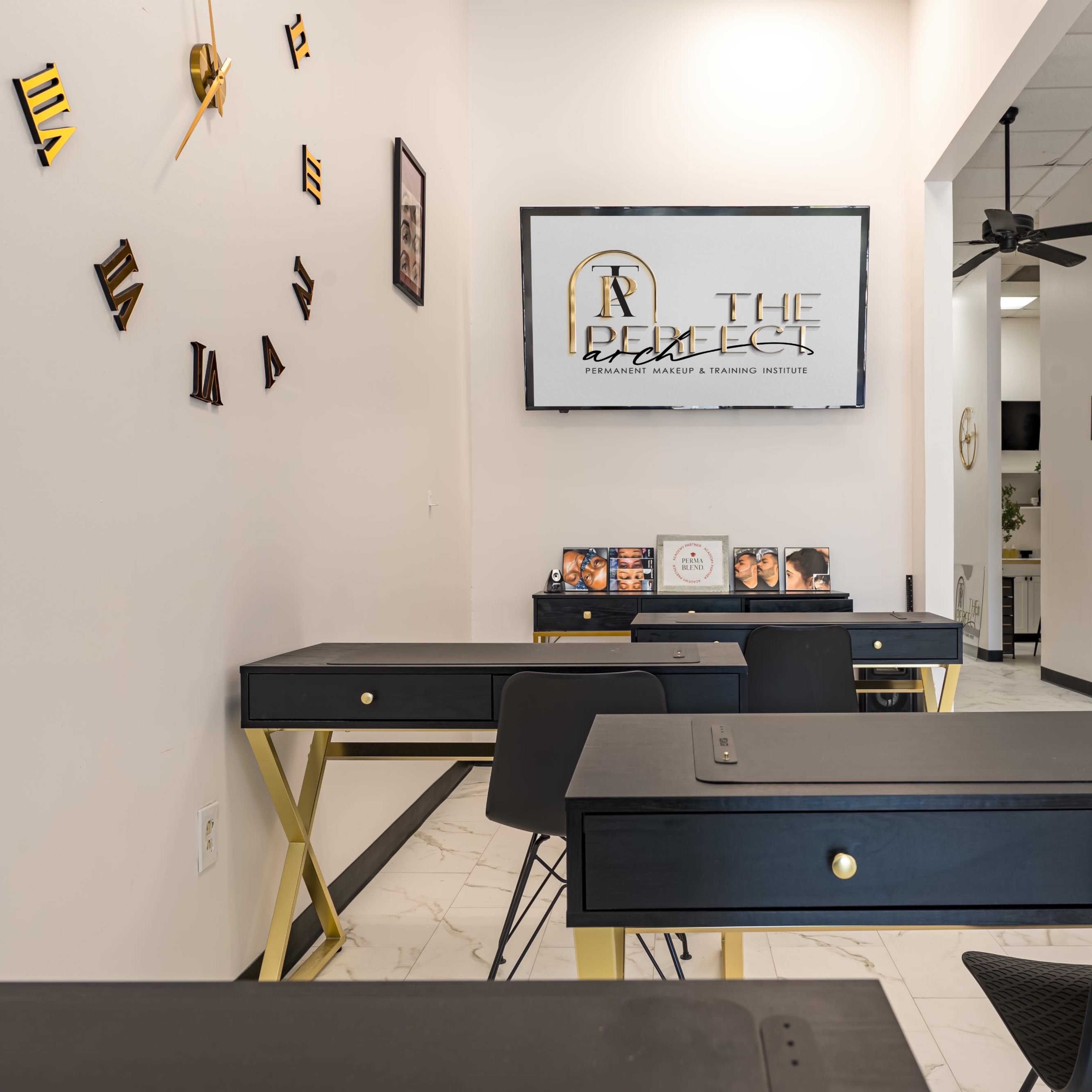 A modern classroom equipped with black desks, a wall-mounted screen displaying a logo, and several framed photos on a desk.