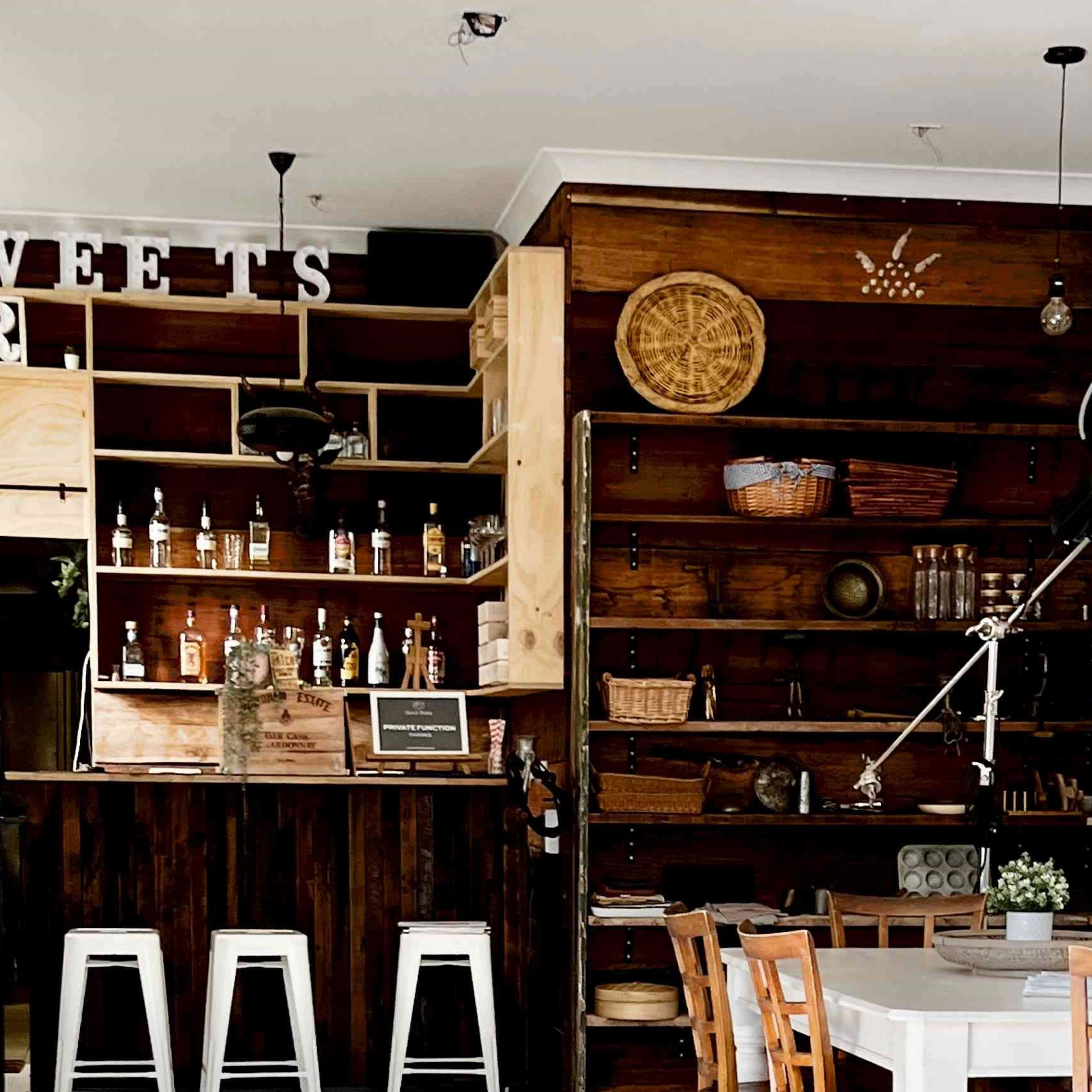 A rustic bar area with wooden shelves displaying bottles and decorative items, accompanied by a white dining table and chairs.