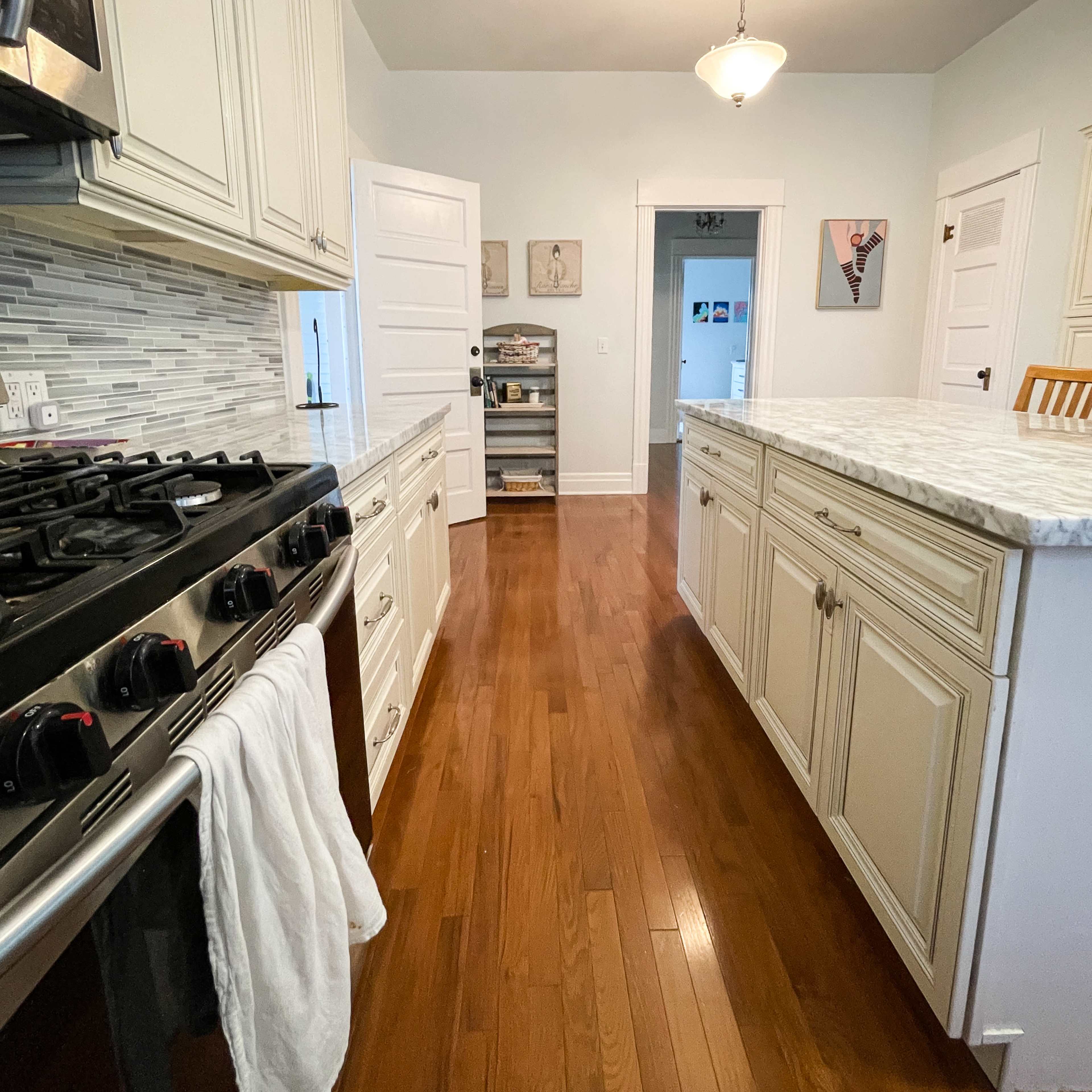A kitchen with white cabinetry, a marble countertop, and wooden flooring, extending into a hallway with doorways.