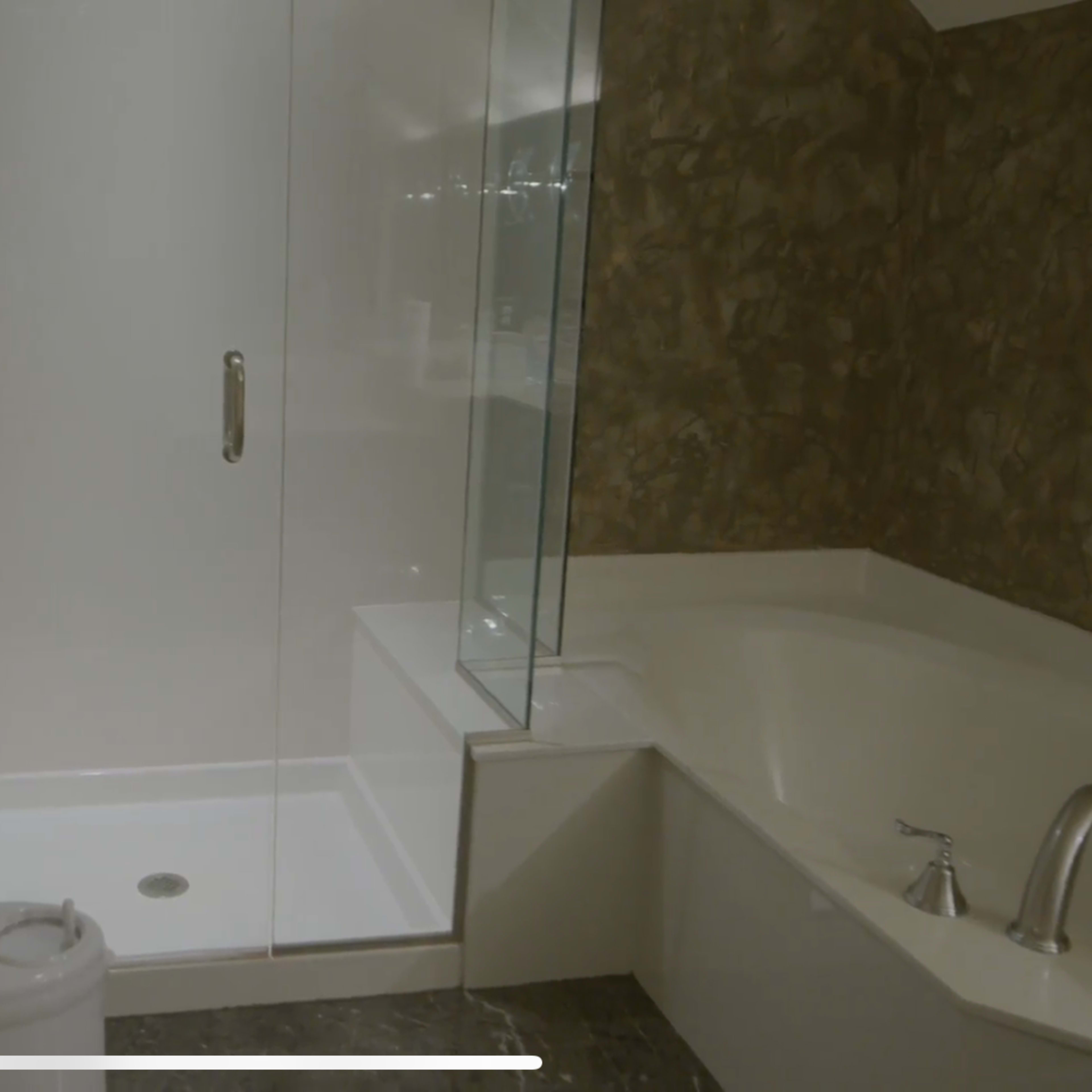 A bathroom with a glass shower unit, a soaking tub, and a toilet on the floor.
