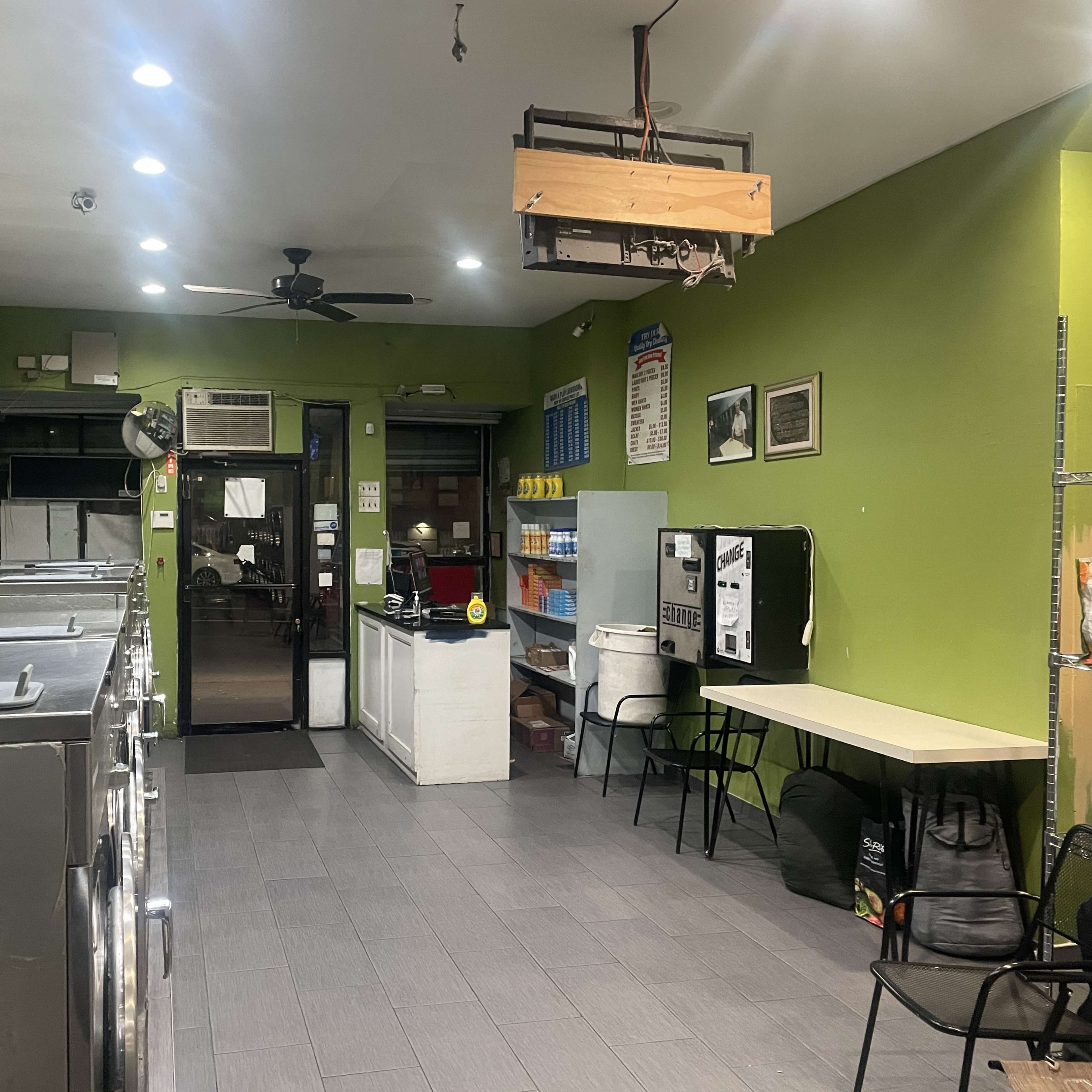 A laundry room with several washing machines on one side, a service counter, and seating against a green wall.