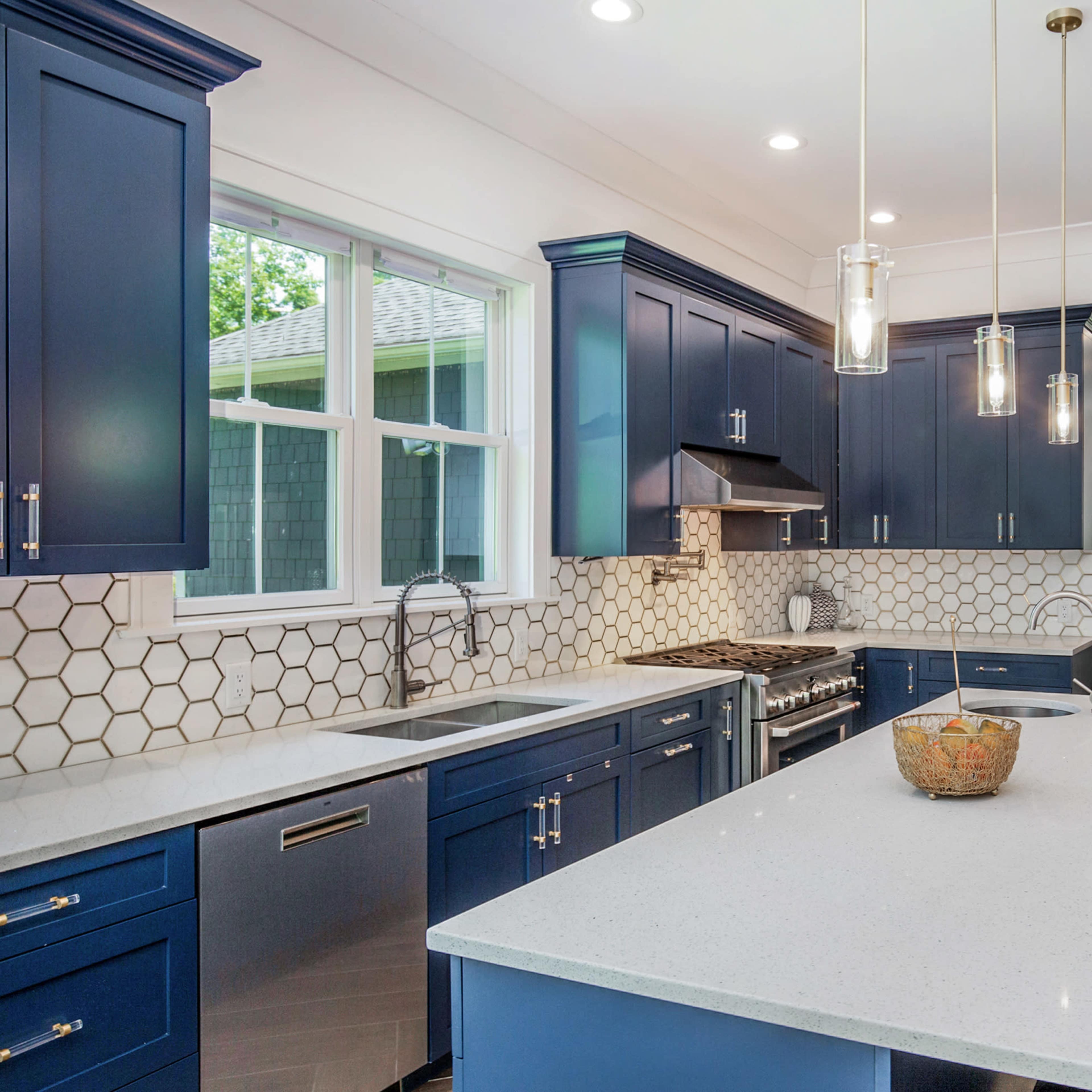 A modern kitchen features navy blue cabinets, a white countertop, and hexagonal tiled backsplashes with a view of an adjoining room.