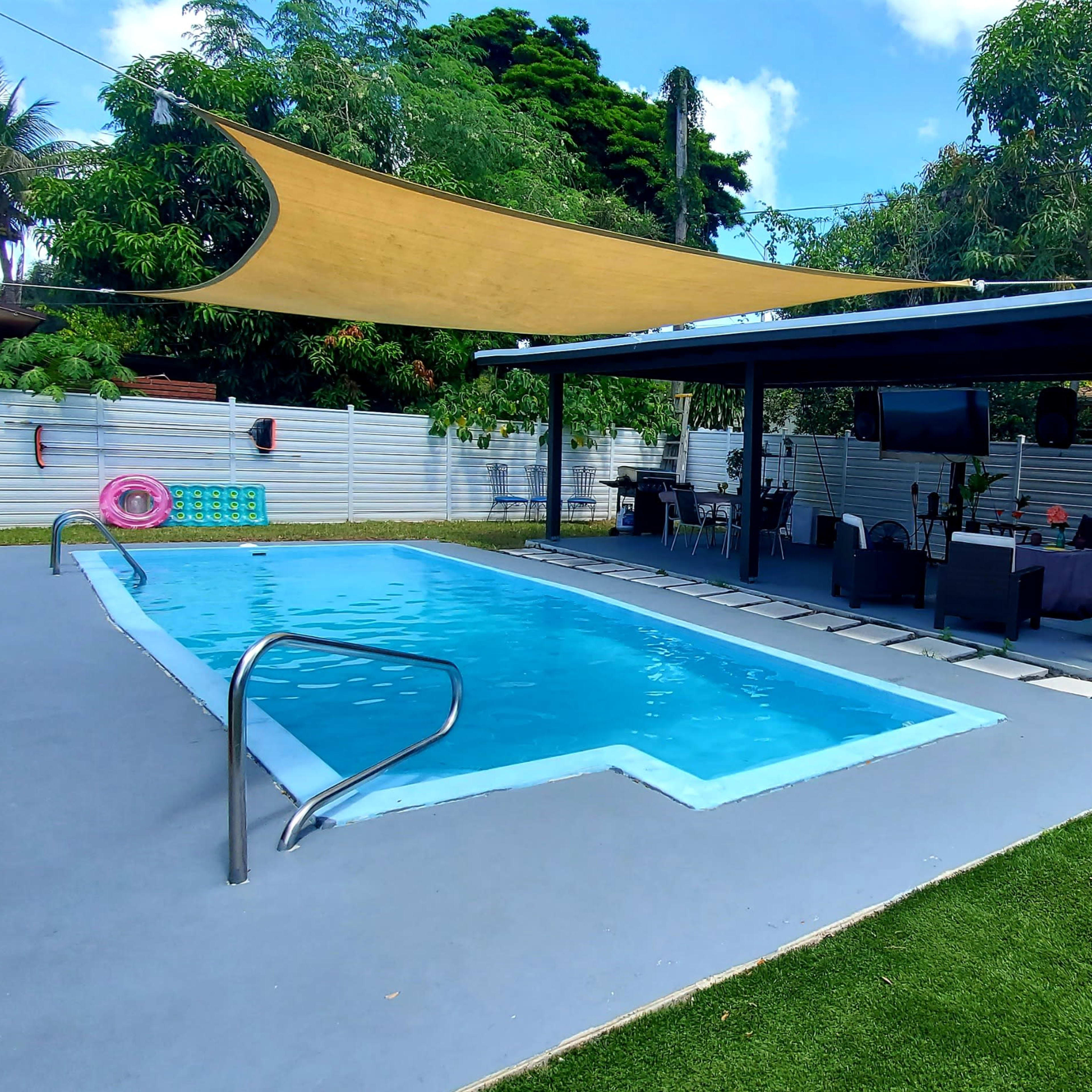 A backyard pool area featuring a rectangular swimming pool, a shaded seating area with outdoor furniture, and a maintained lawn.