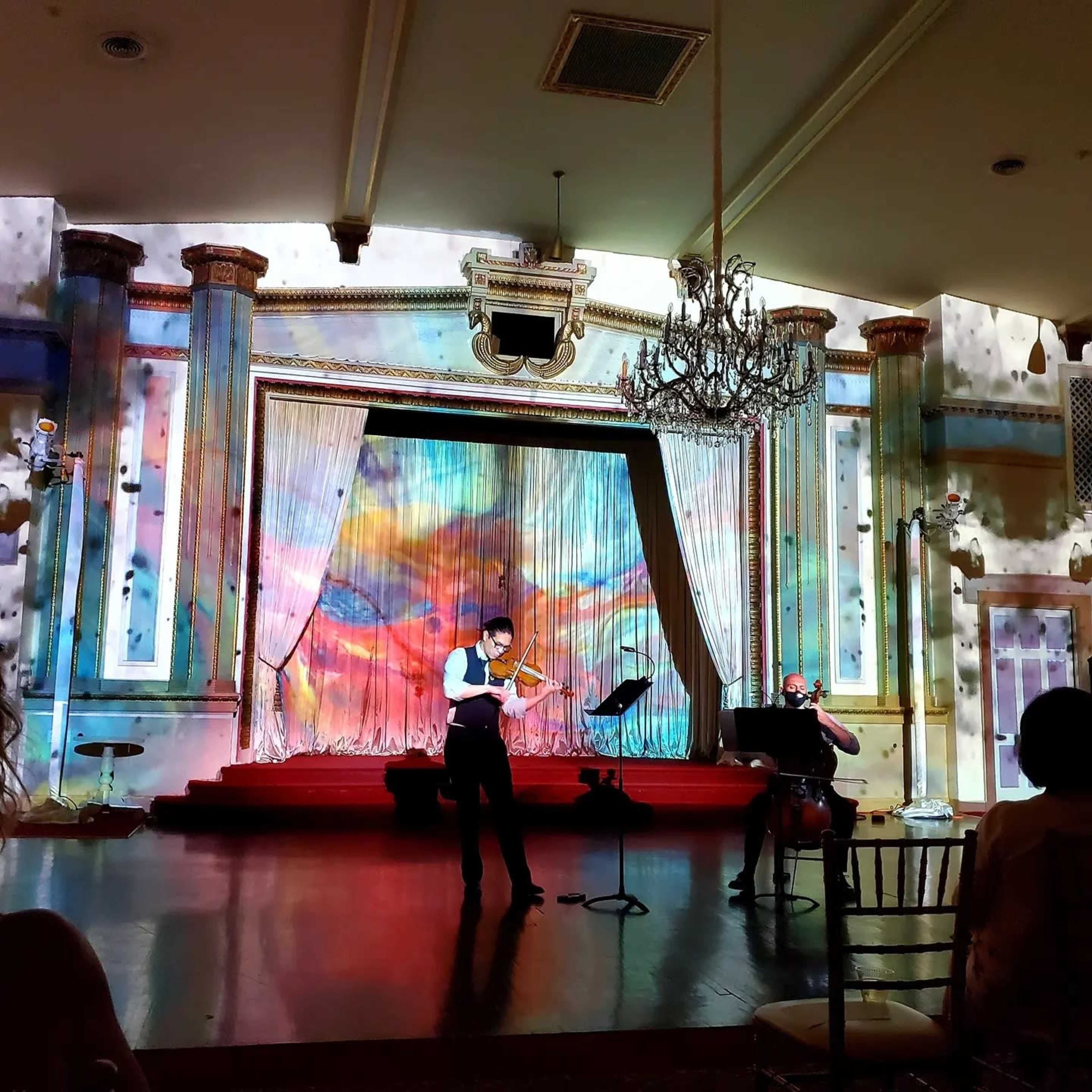 A violinist performs on stage in front of a colorful, projected backdrop in an elegantly decorated venue.
