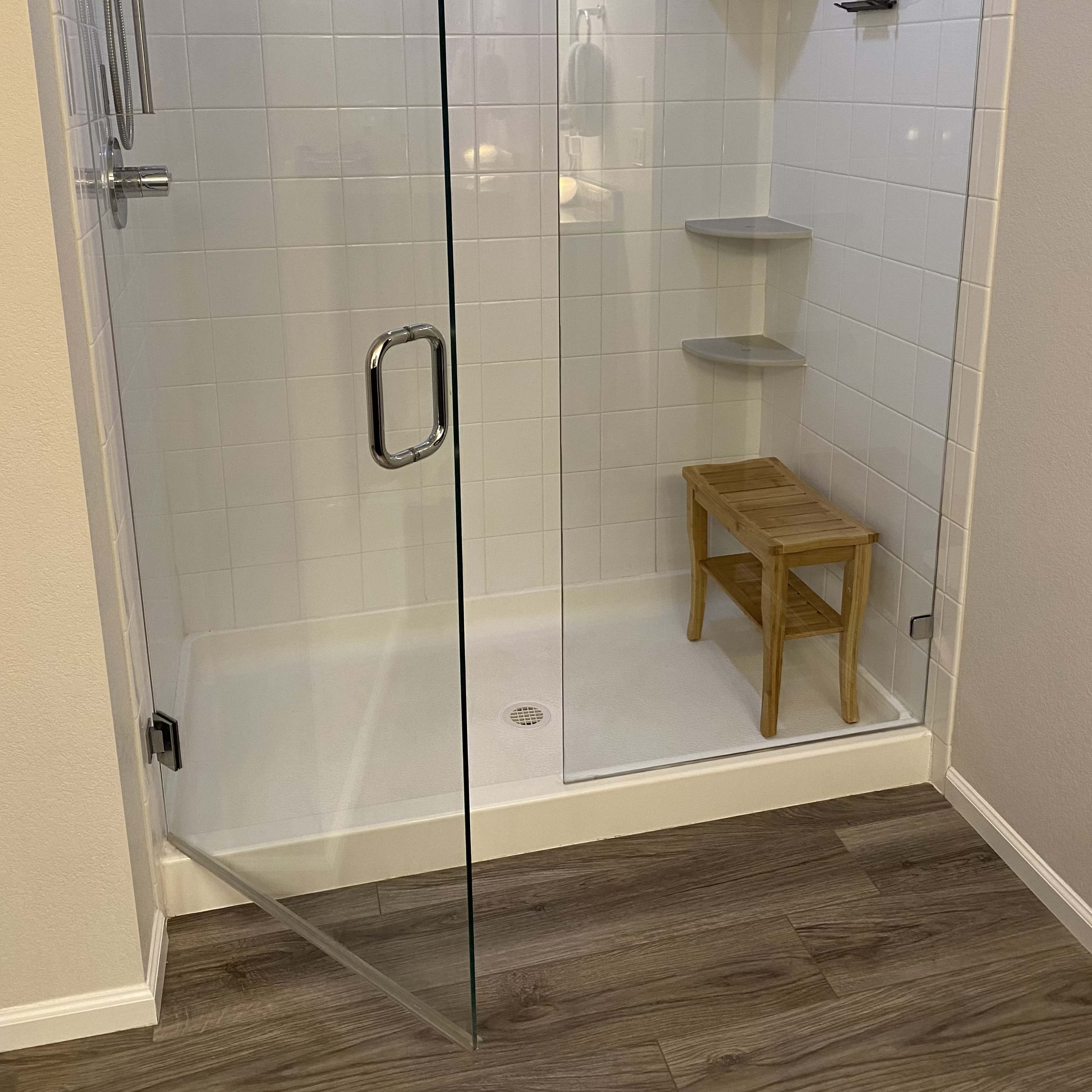 A modern shower stall with a glass door, tiled walls, a wooden stool, and built-in shelves.