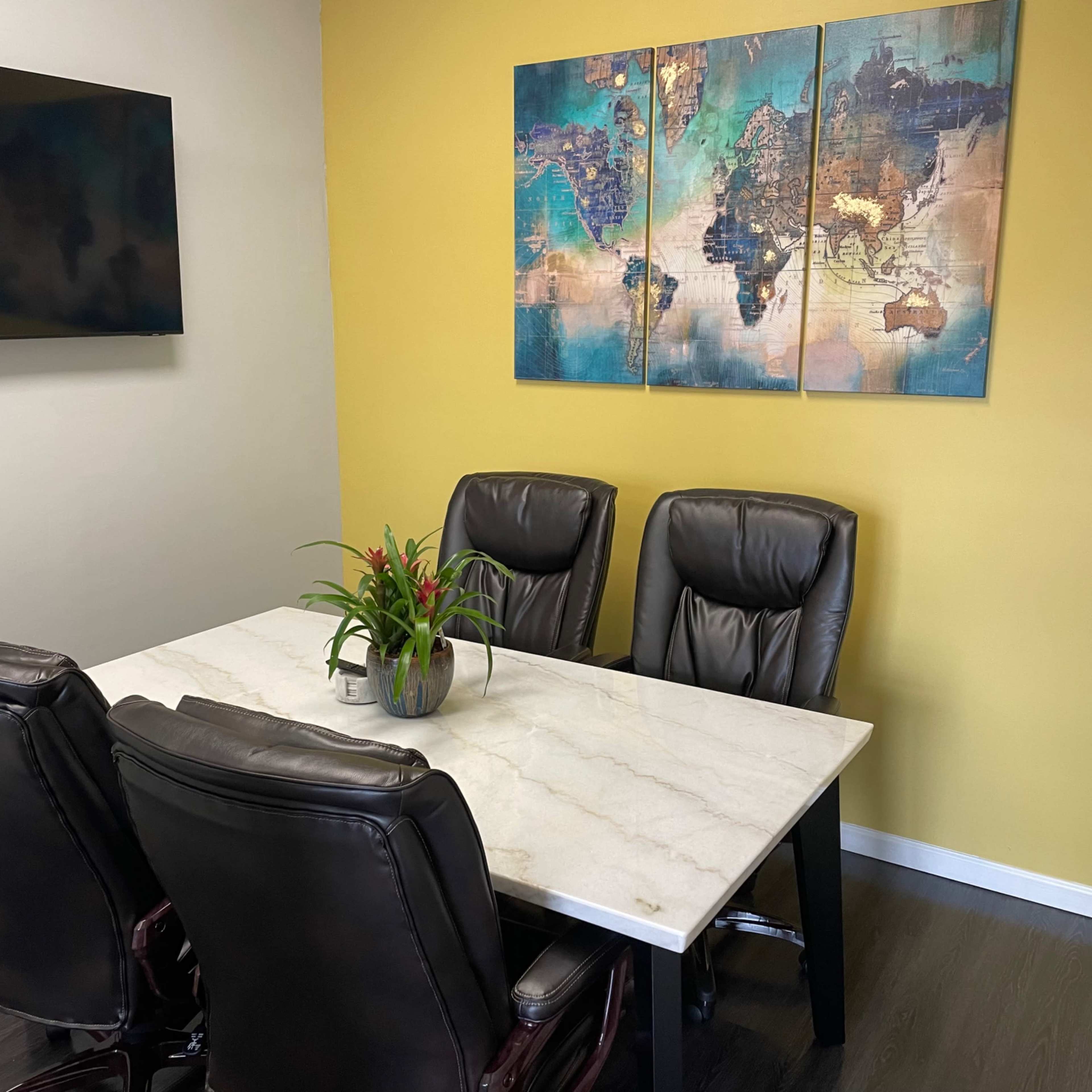 A small meeting room features a marble-topped table surrounded by four black leather chairs and a wall-mounted television, with a colorful world map artwork above.