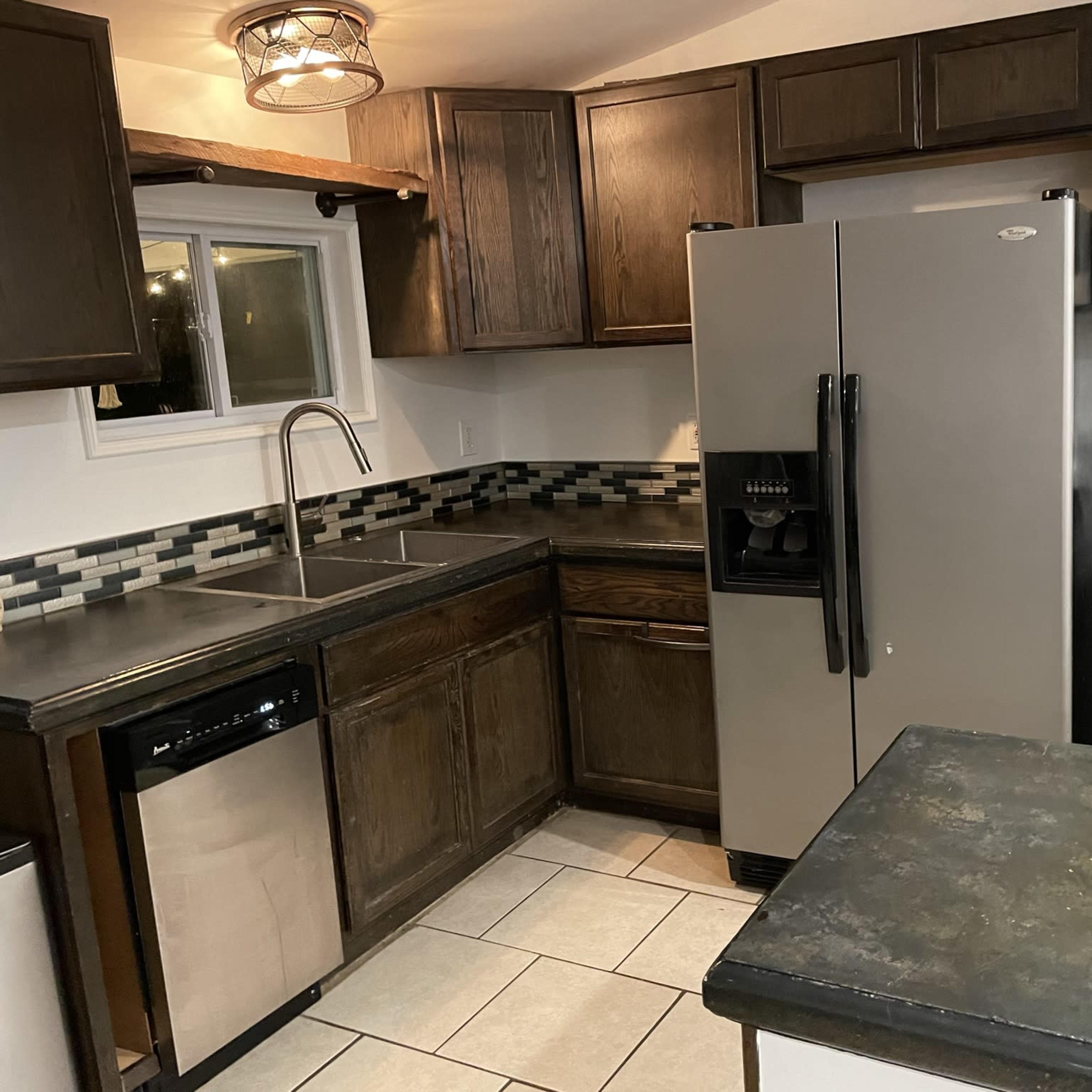 A kitchen with dark wooden cabinets, stainless steel appliances, a double sink, and a tiled backsplash.