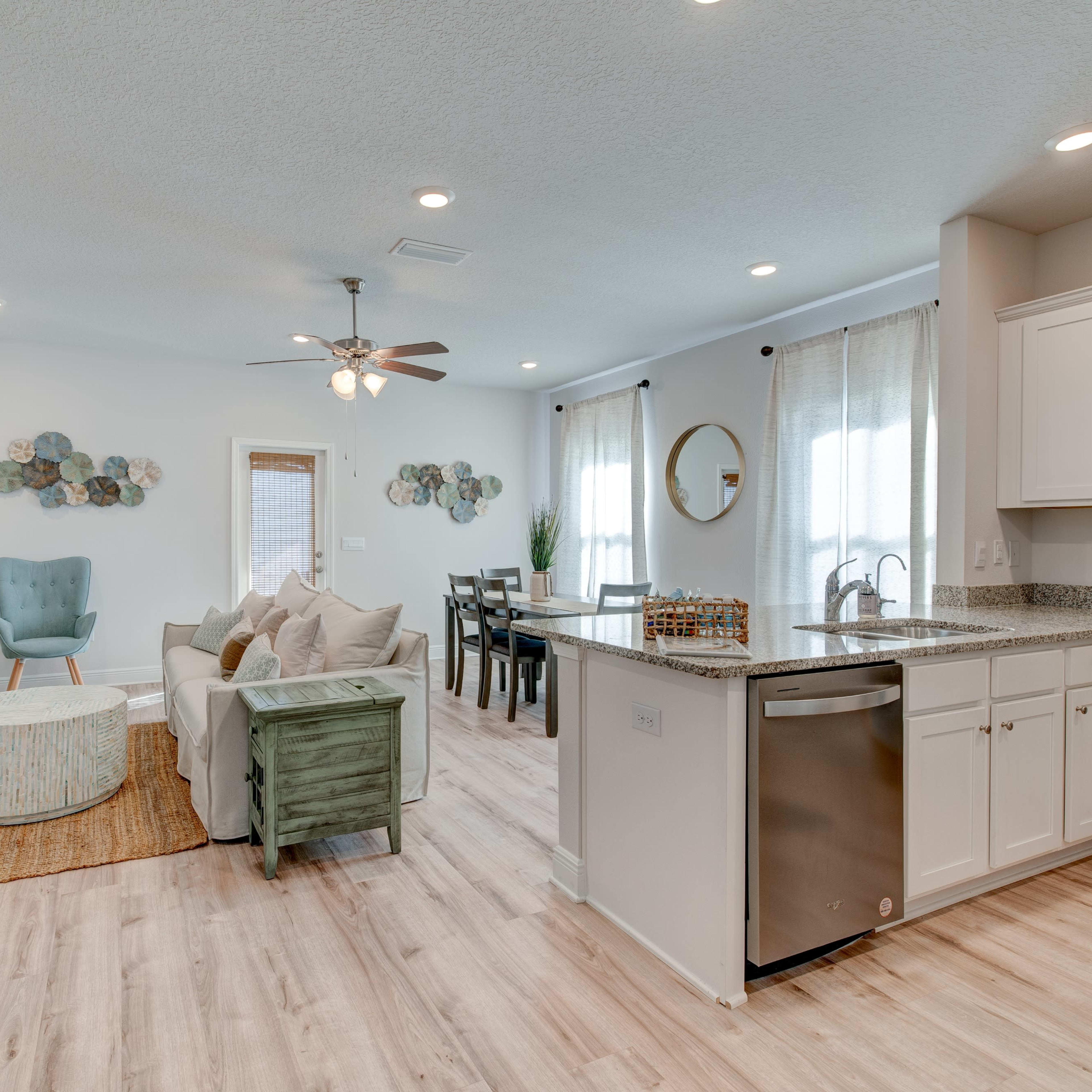 A brightly lit open-concept living area with a kitchen, dining space, and seating arrangement featuring modern furnishings and decorative elements.