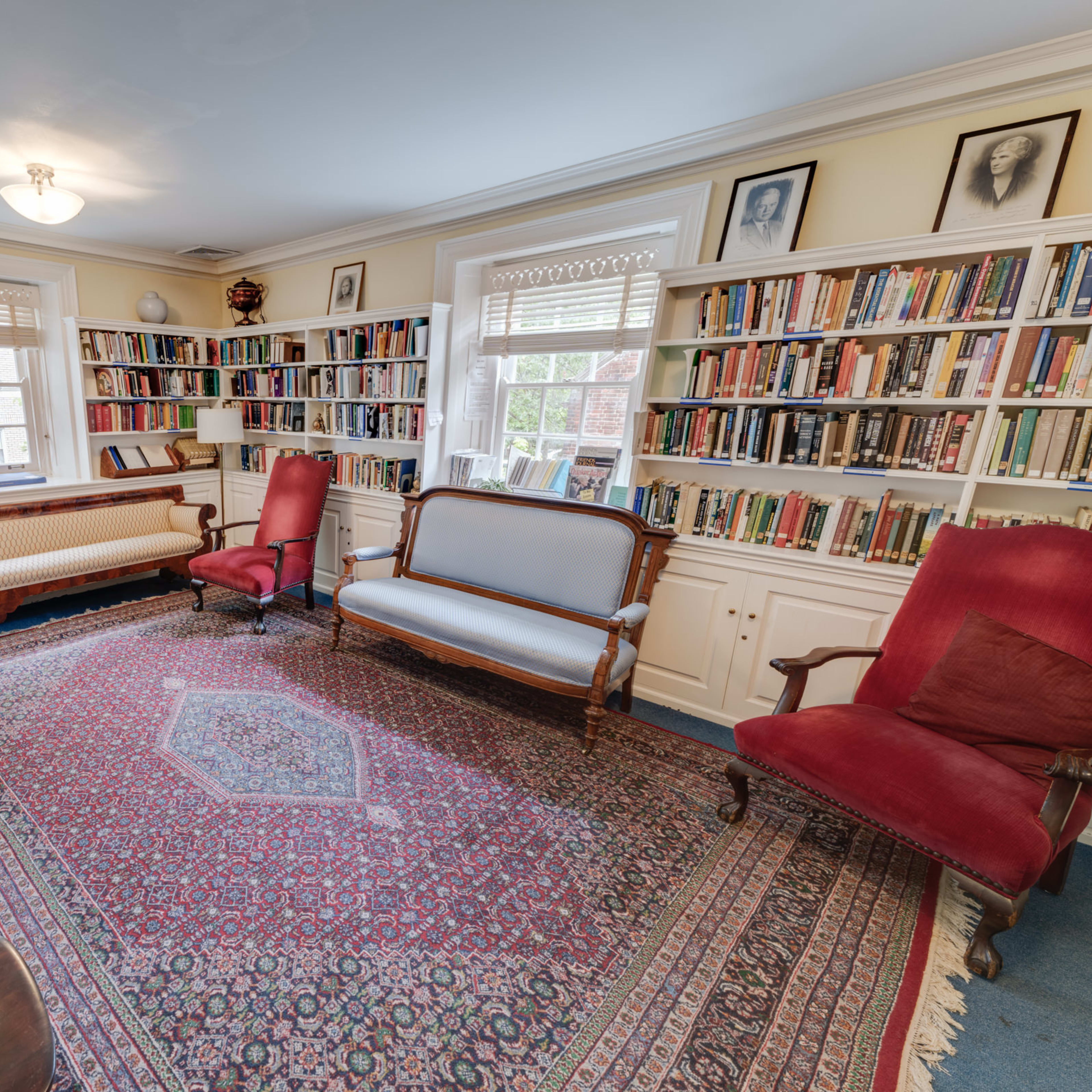 A cozy library with several seating options arranged around a patterned rug and lined with bookshelves full of books.