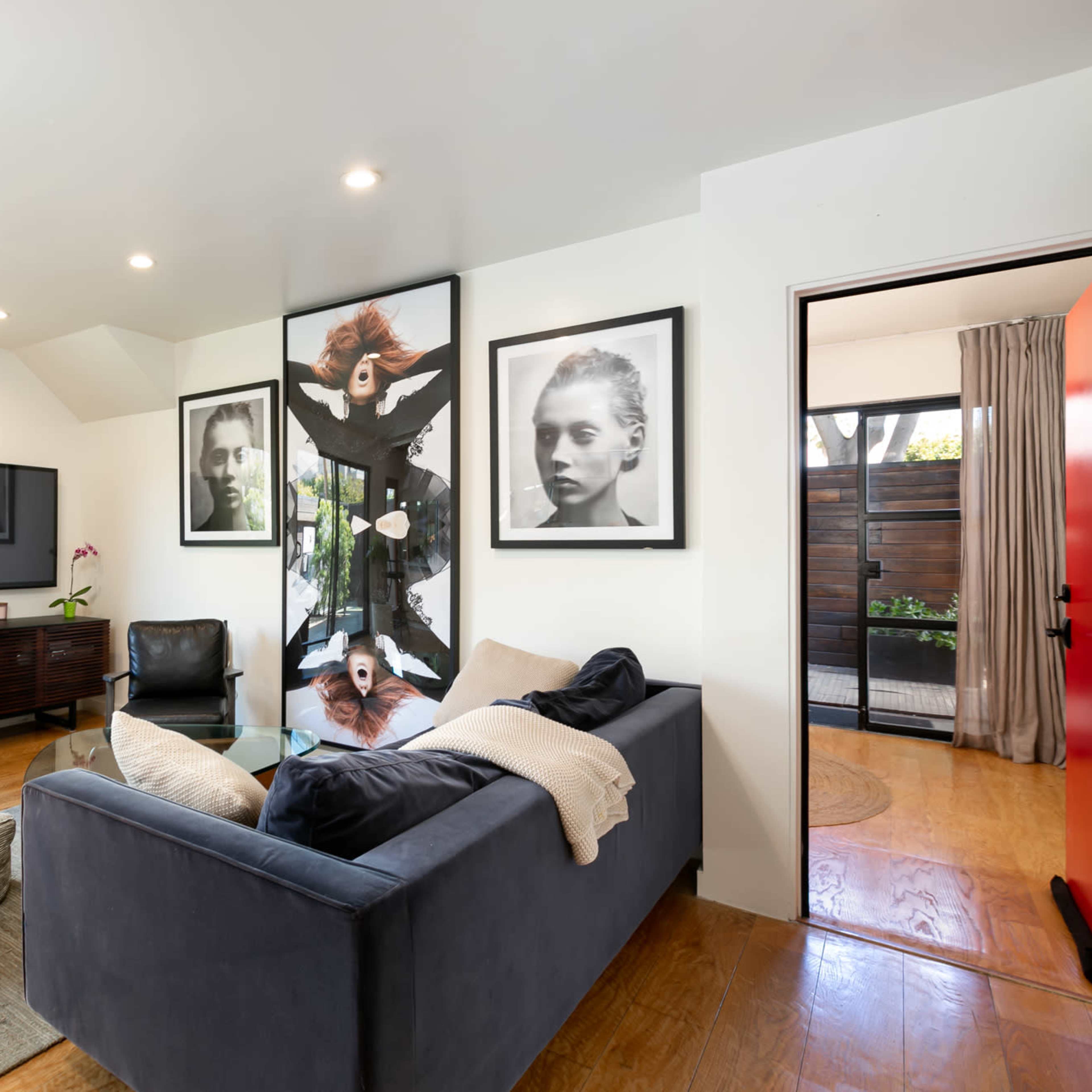 A modern living room with a dark sofa, a wooden TV unit, and black-and-white framed portraits on the wall.