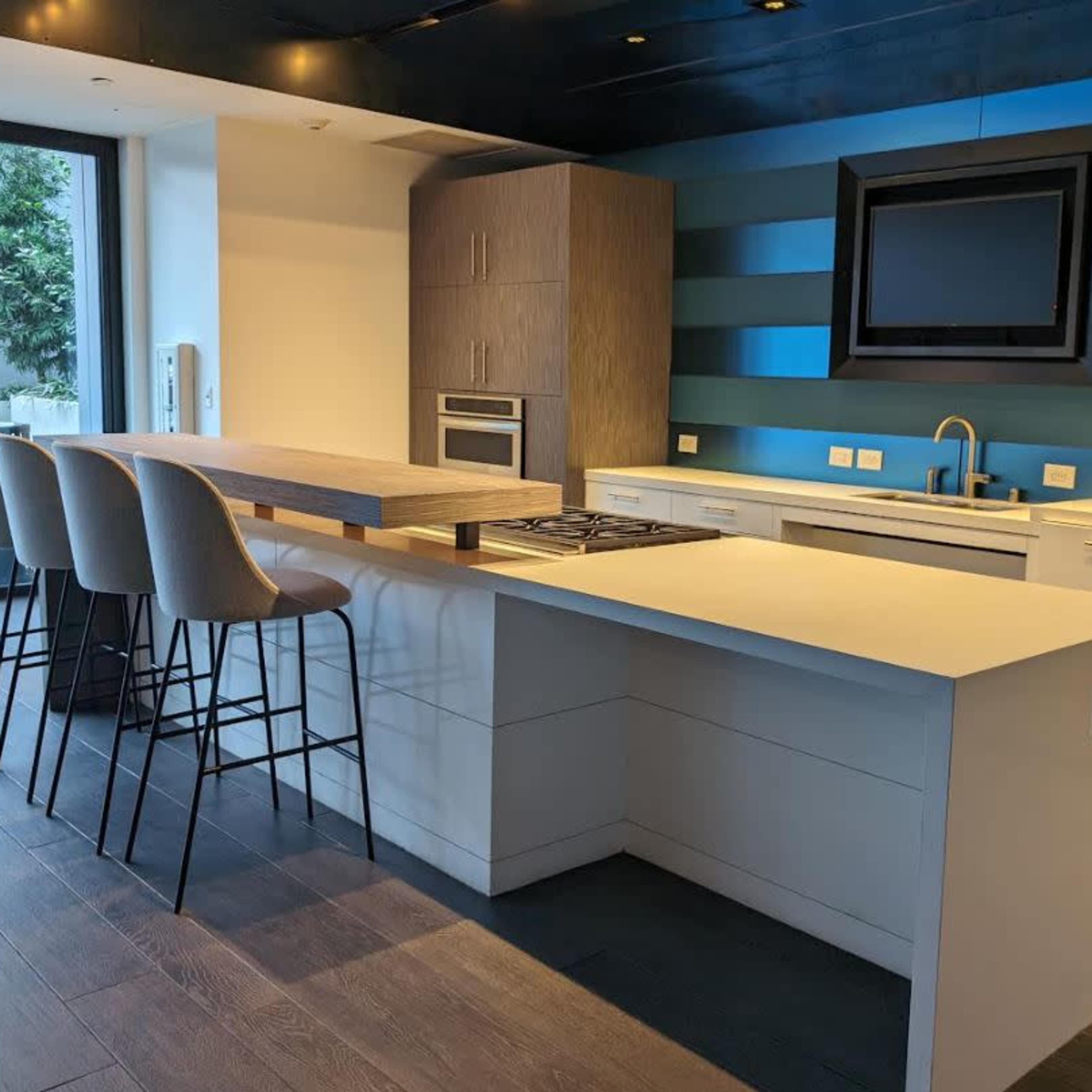 A modern kitchen with a central island, bar seating, and sleek cabinetry under a dark ceiling with blue accent walls.