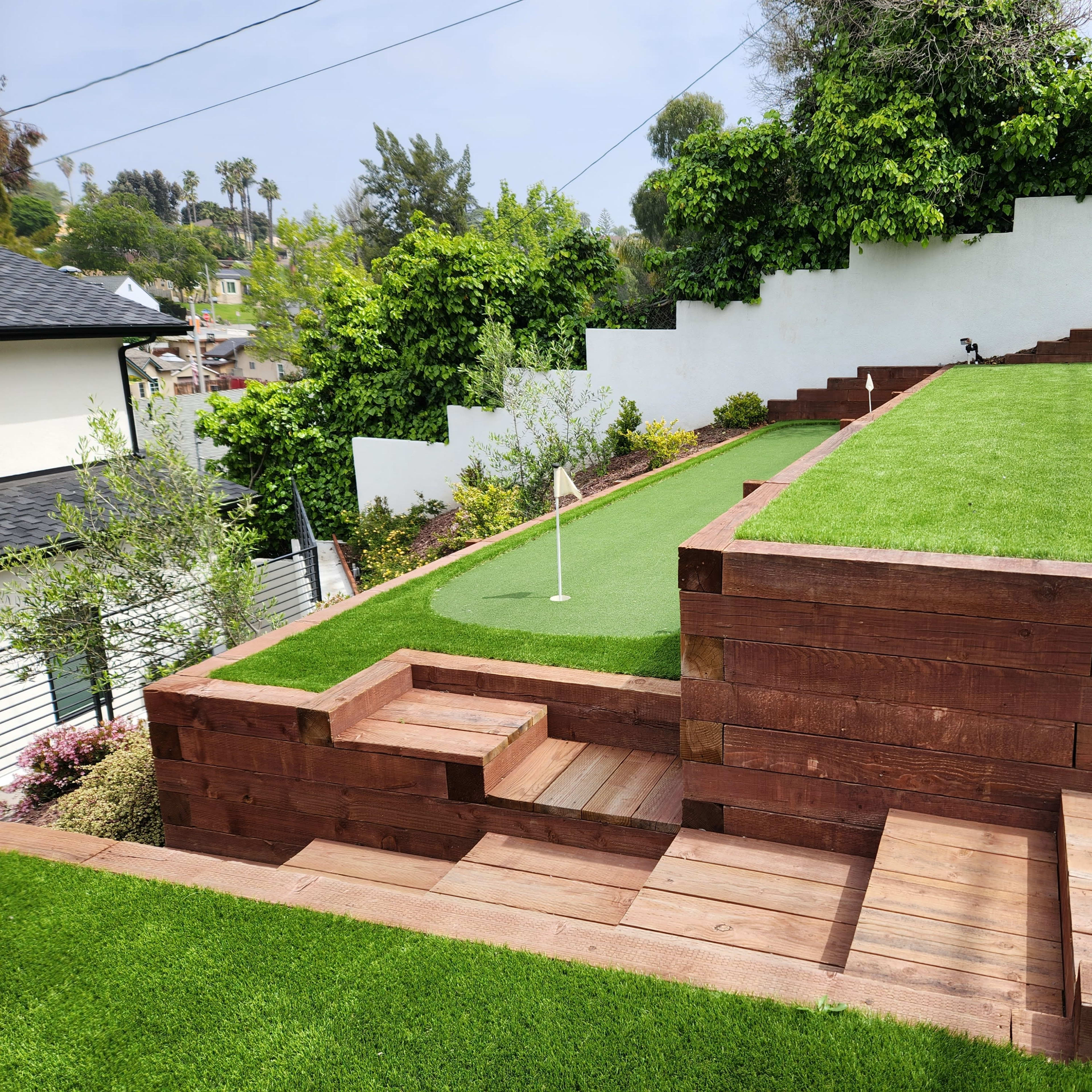 A landscaped outdoor area featuring two levels of artificial grass, bordered by wooden retaining walls and steps.