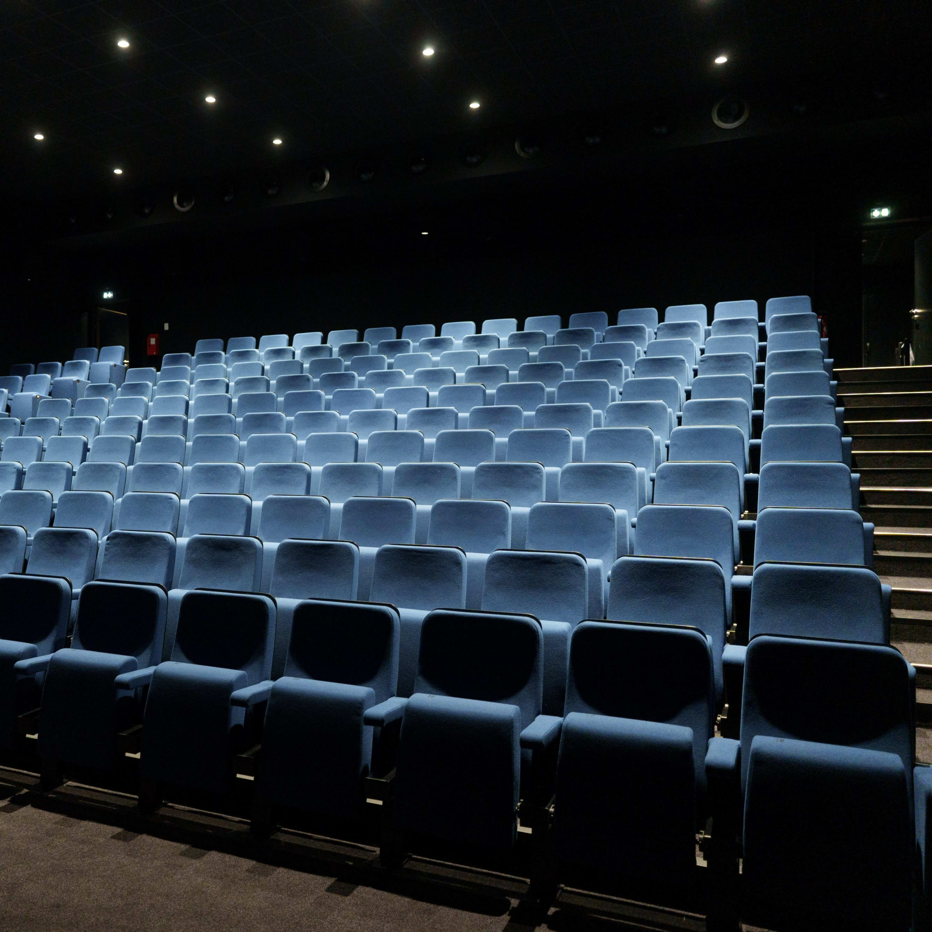 A nearly empty movie theater with rows of blue upholstered seats arranged in a sloped format.