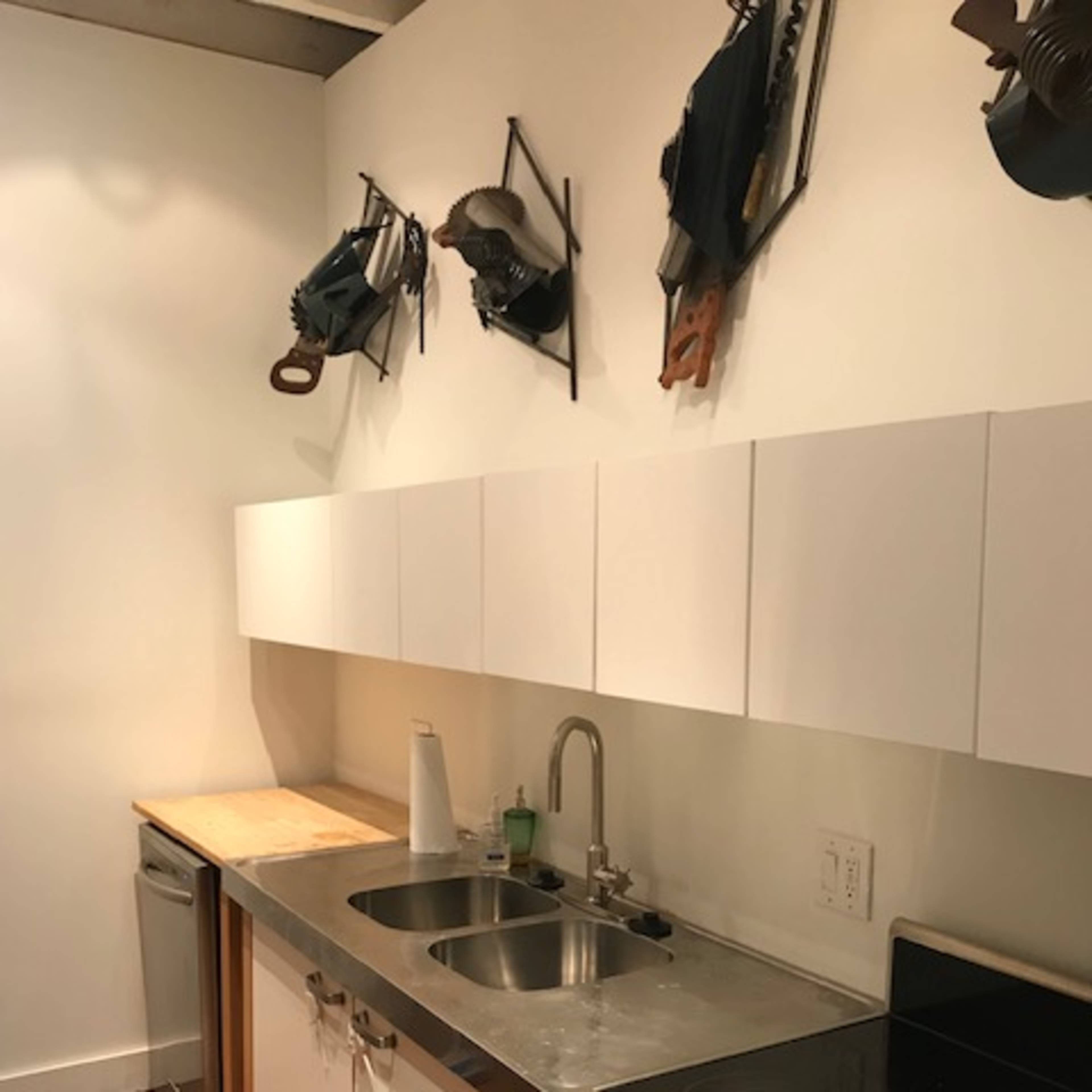 A modern kitchen equipped with a sink, stove, and cabinetry, featuring wooden flooring and wall-mounted kitchen tools.
