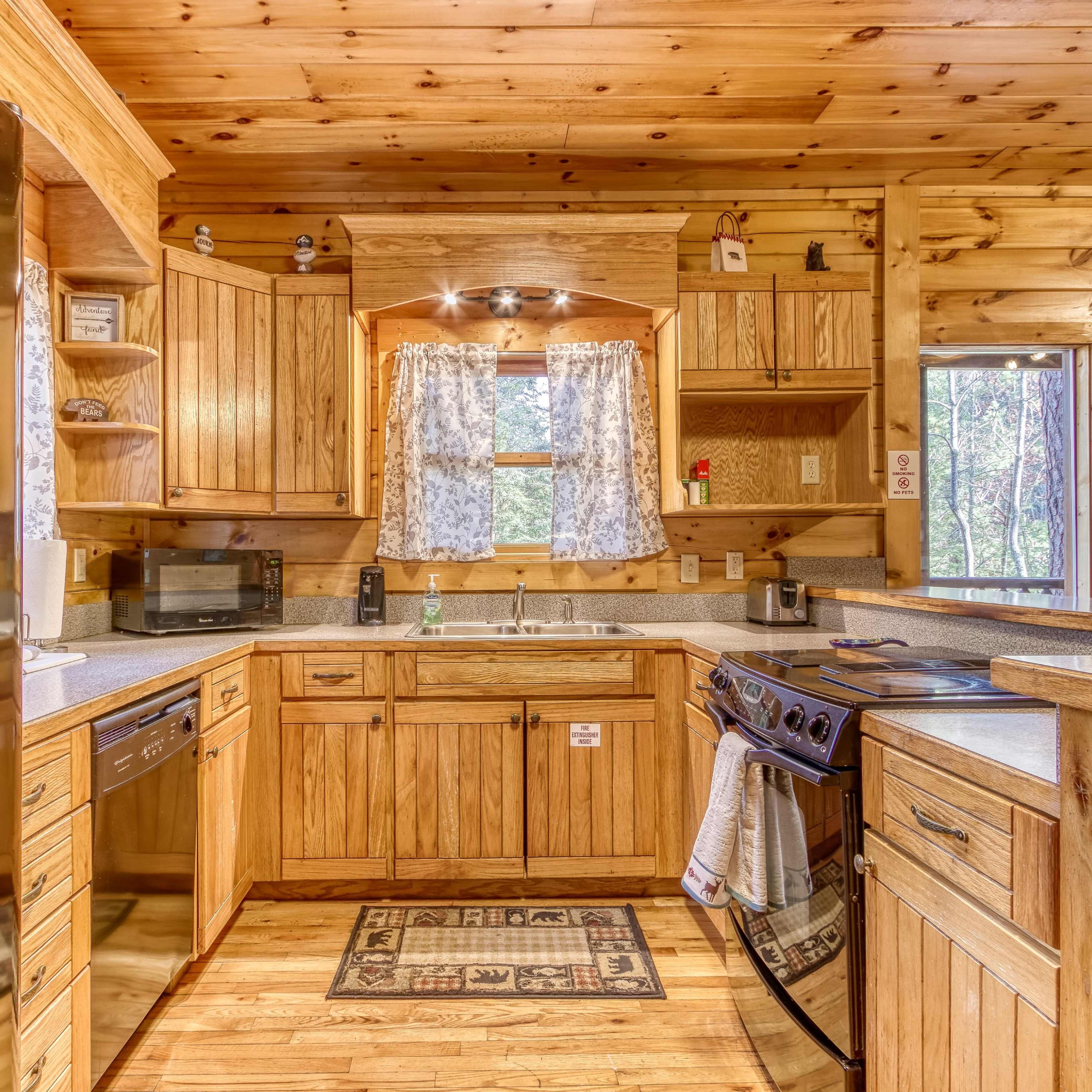 A wooden cabin kitchen with light wood cabinets, a stove, and a window offering a view of the outdoors.