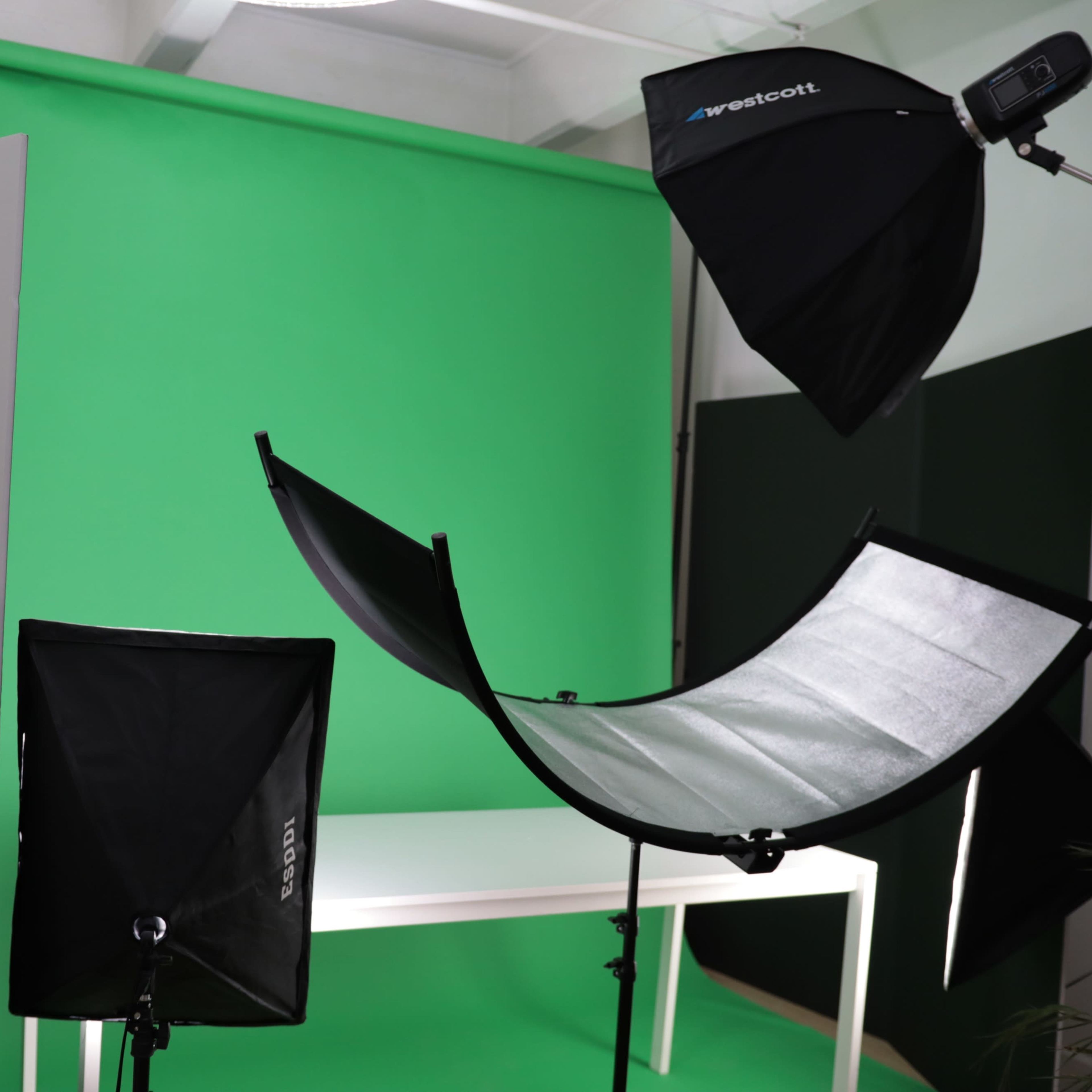 A photography studio setup featuring a green backdrop, multiple light sources, and a white table.