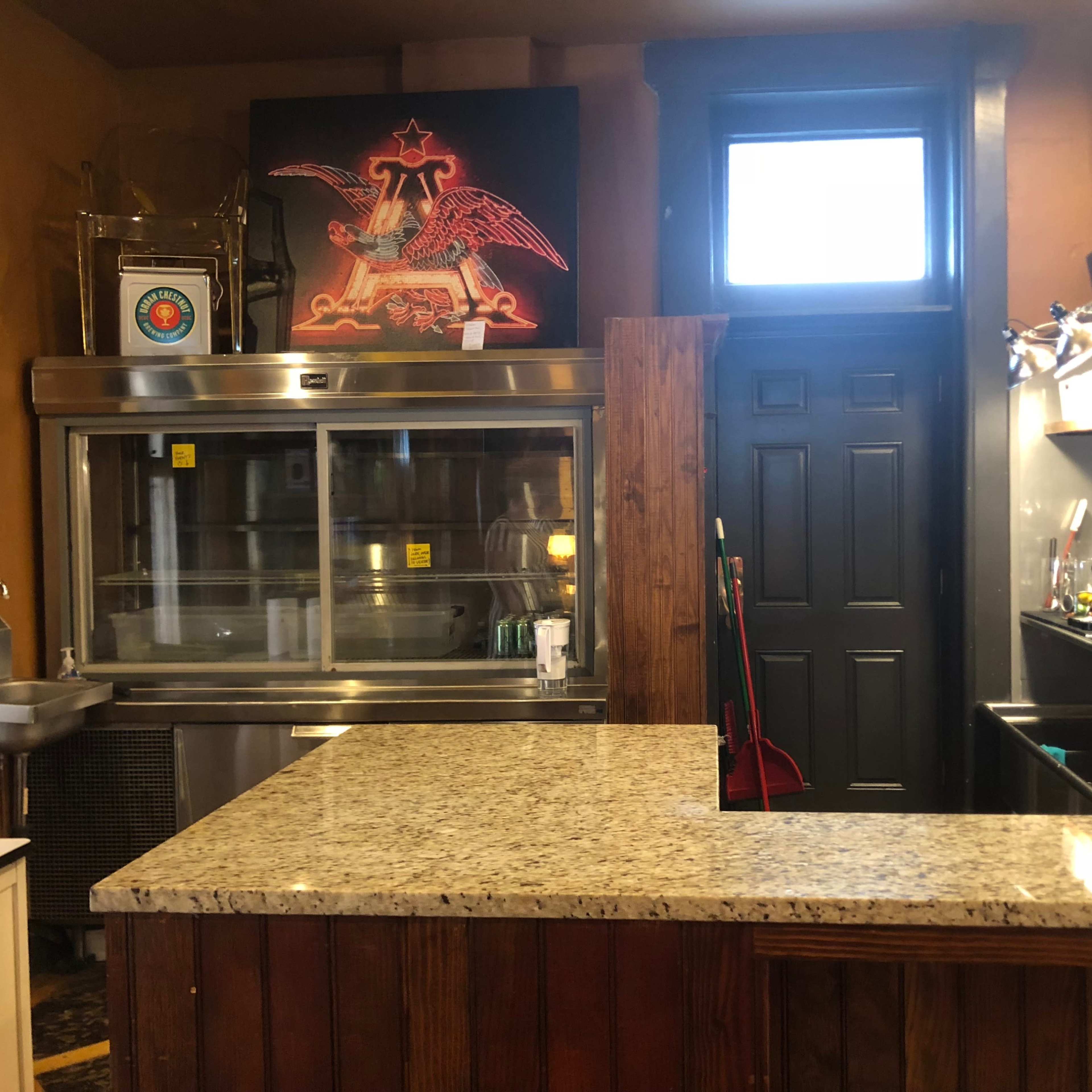 A restaurant interior featuring a granite countertop, an open display refrigerator, a sink, and a black door with a window.