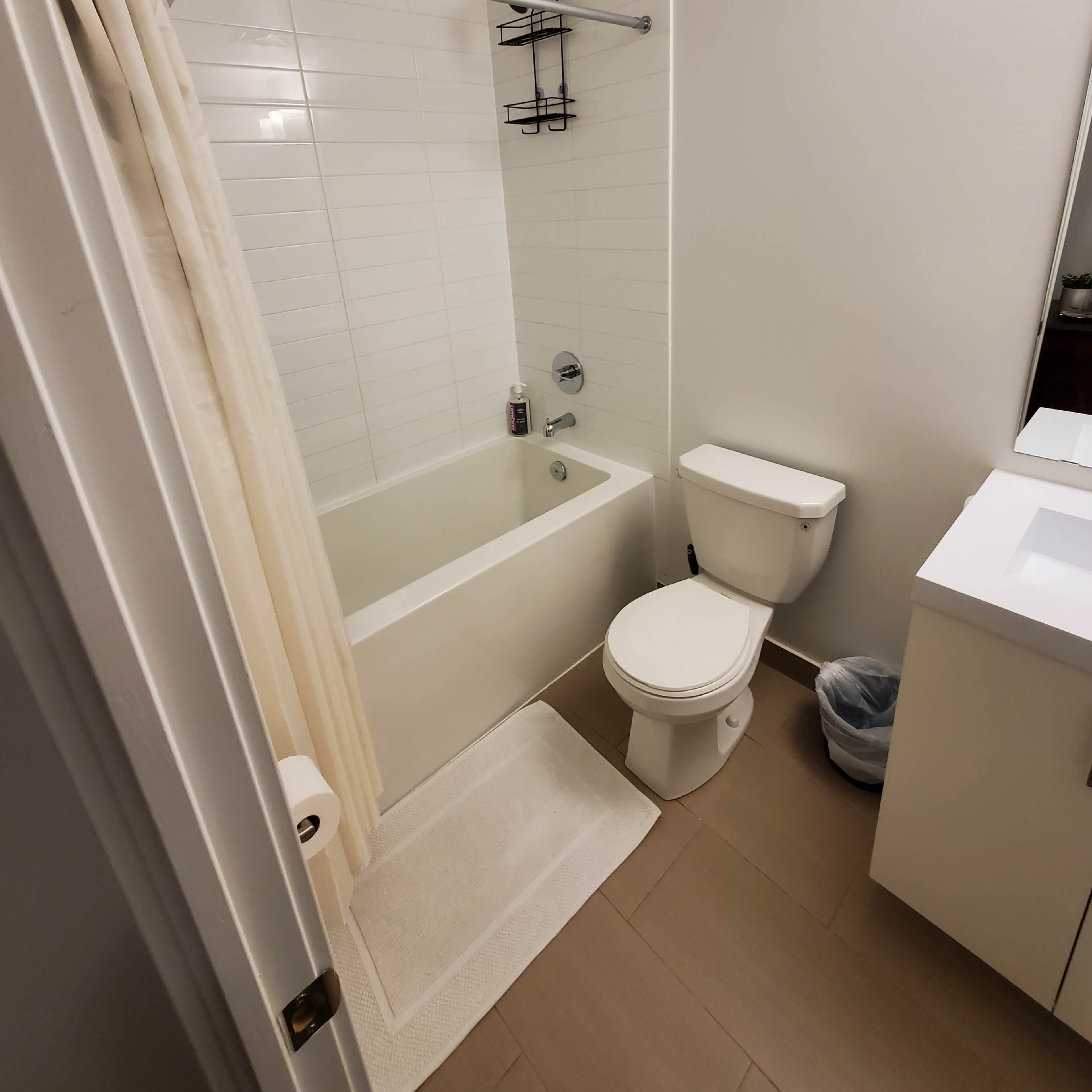 A bathroom with a bathtub, a toilet, a small vanity with a sink, and beige tile flooring.