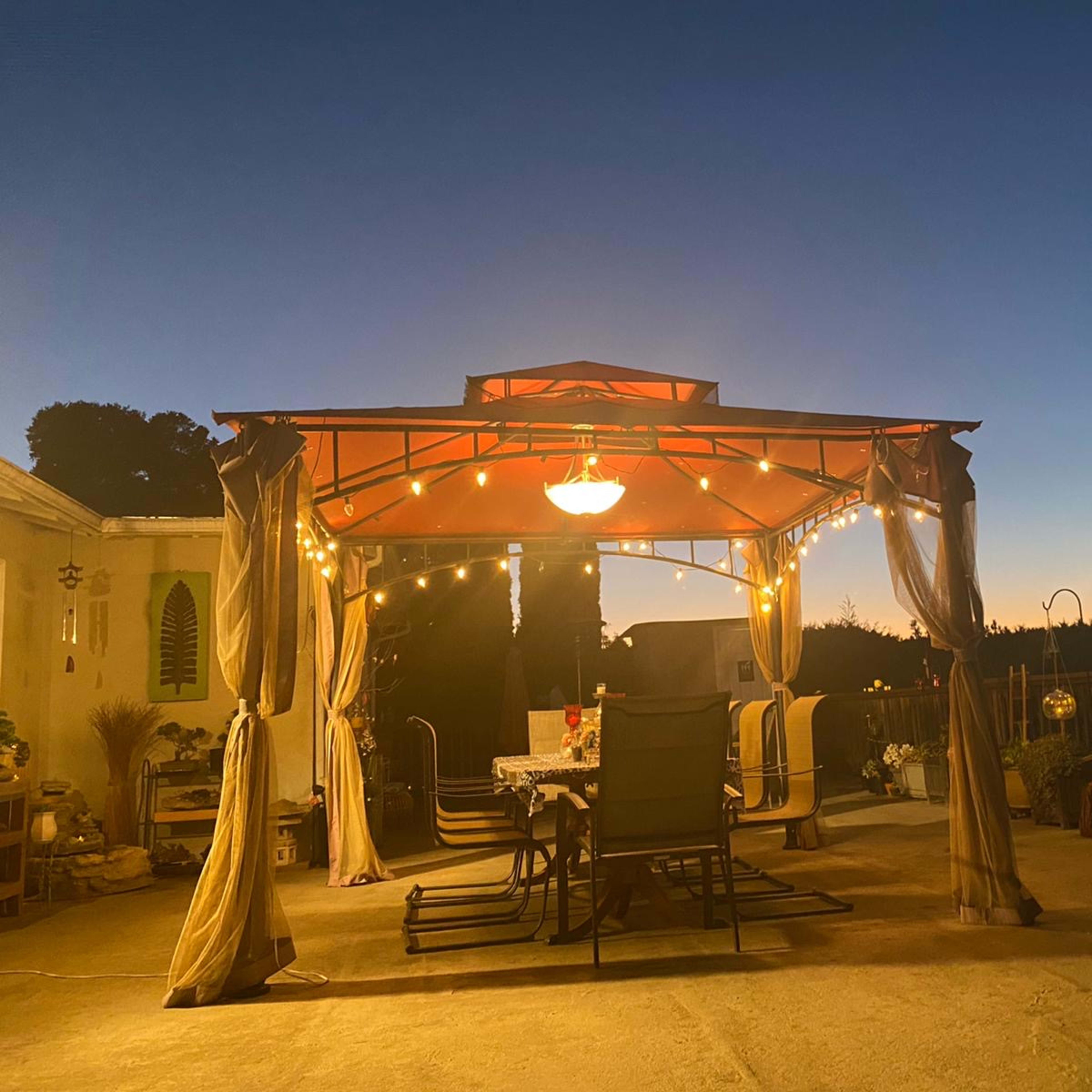 A gazebo with string lights is set up on a patio, overlooking a horizon at dusk.