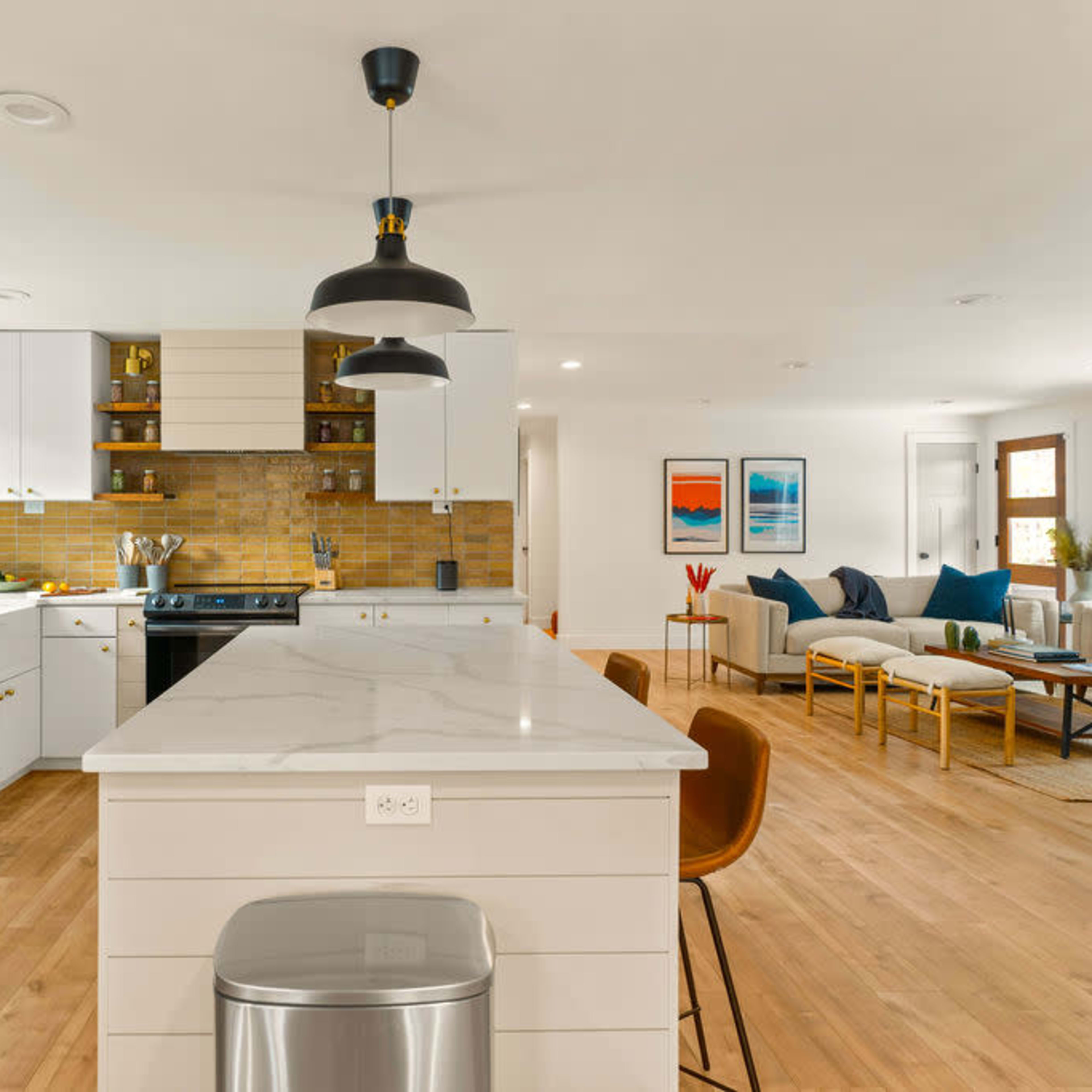 A modern kitchen with a central island and a black refrigerator, featuring white cabinets and a warm-toned backsplash.