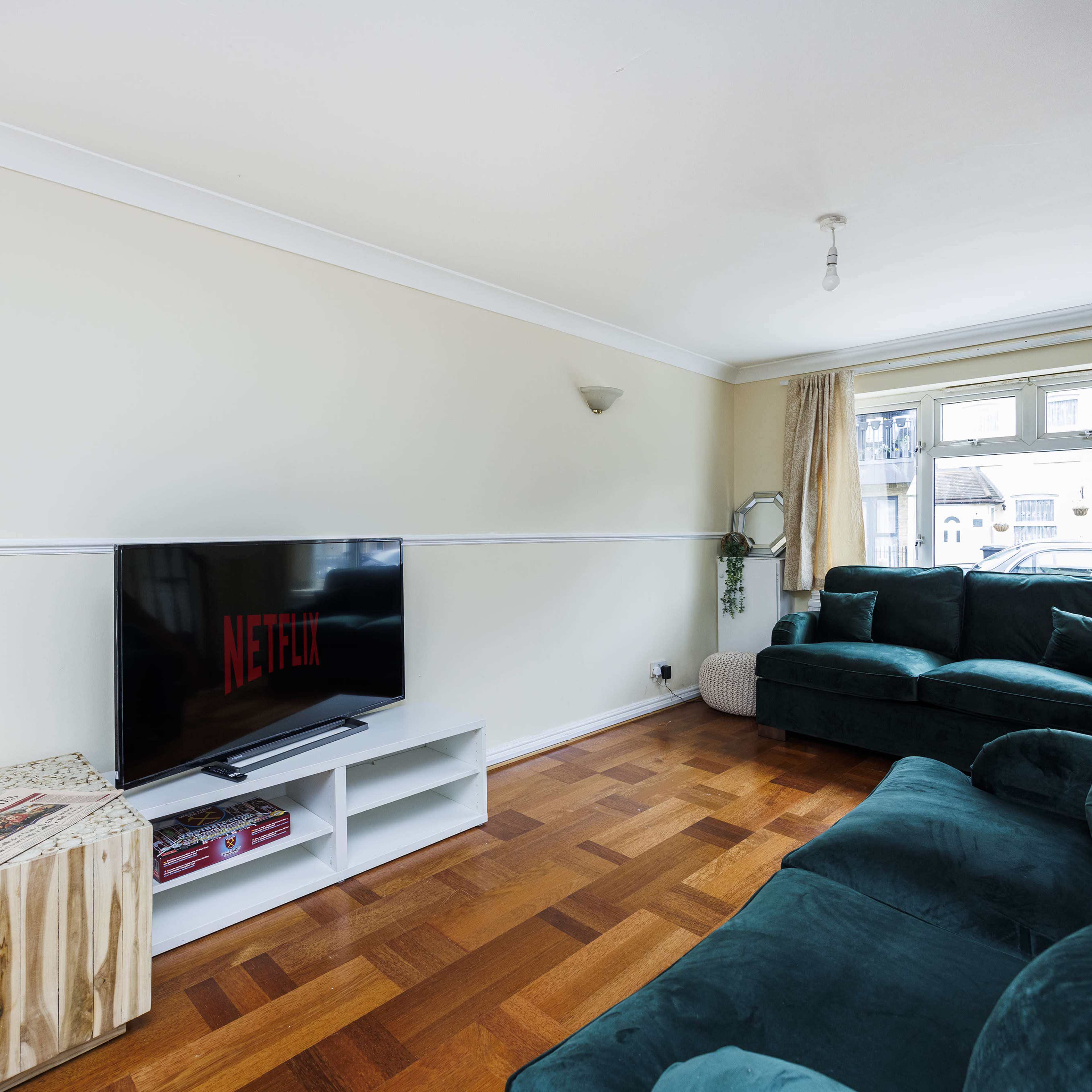 A living room features a green sofa, a wooden coffee table, and a television displaying the Netflix logo.