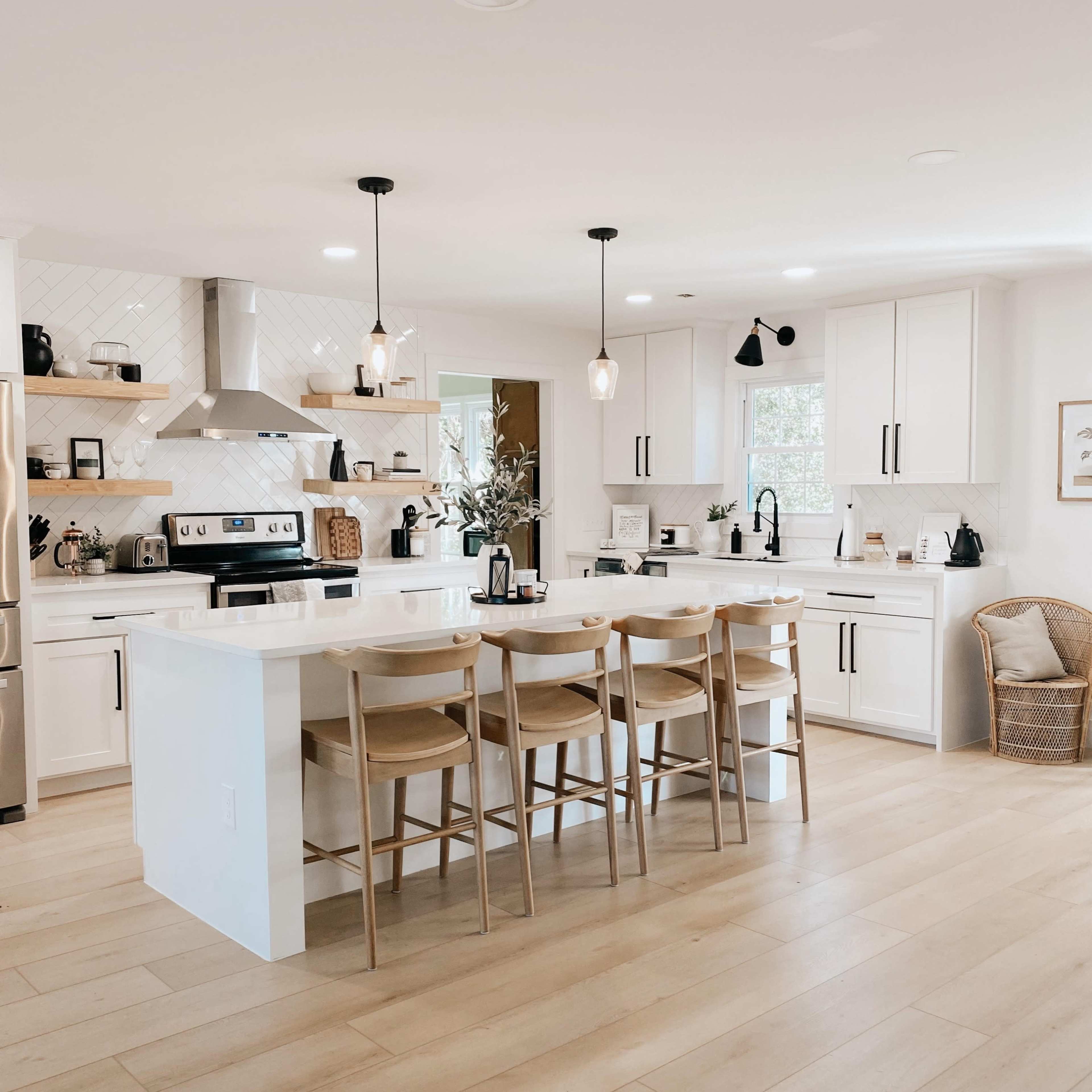 A modern kitchen features white cabinetry, a central island with seating, and stainless steel appliances.