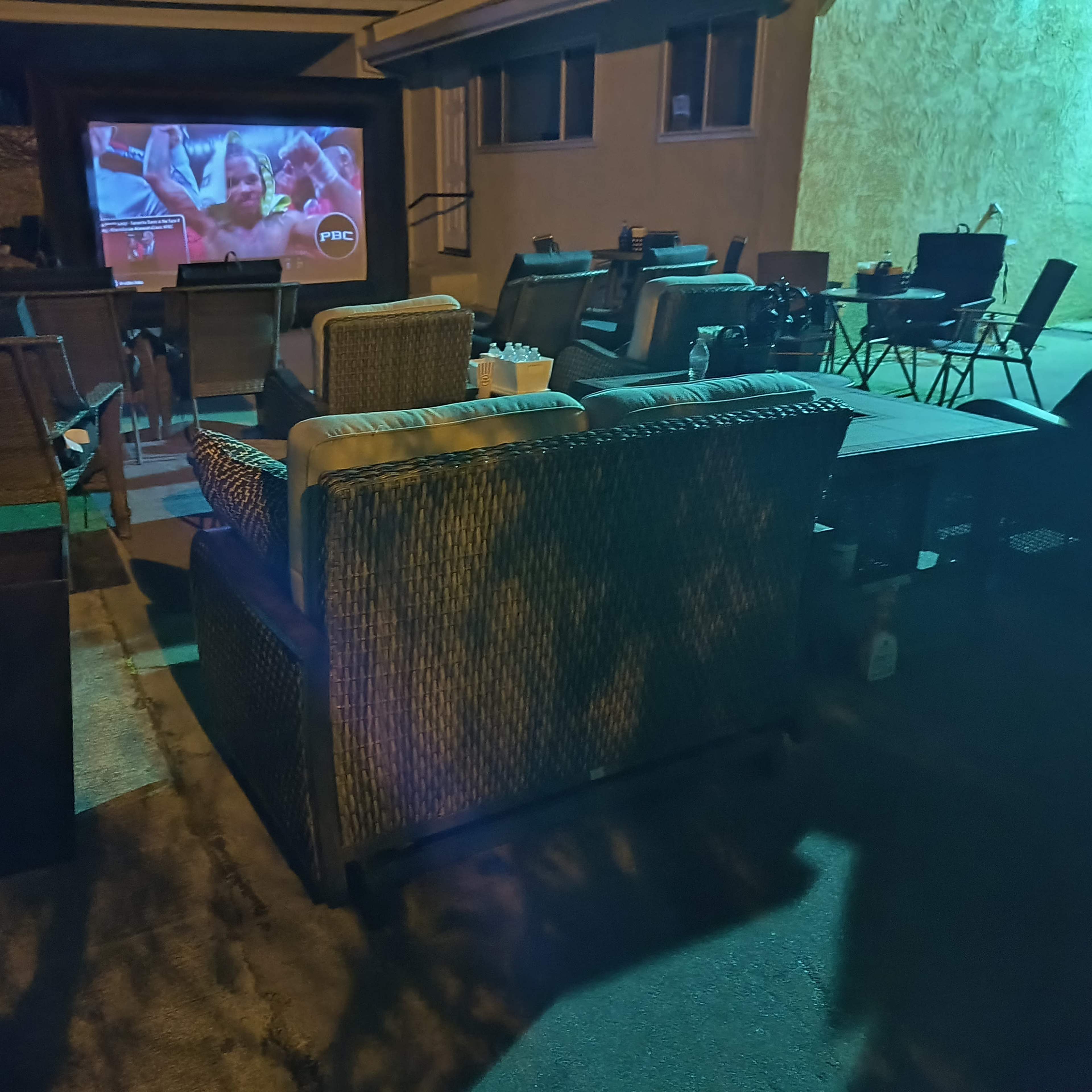 An outdoor seating area with chairs and a couch facing a large screen displaying a movie or program against a wall.