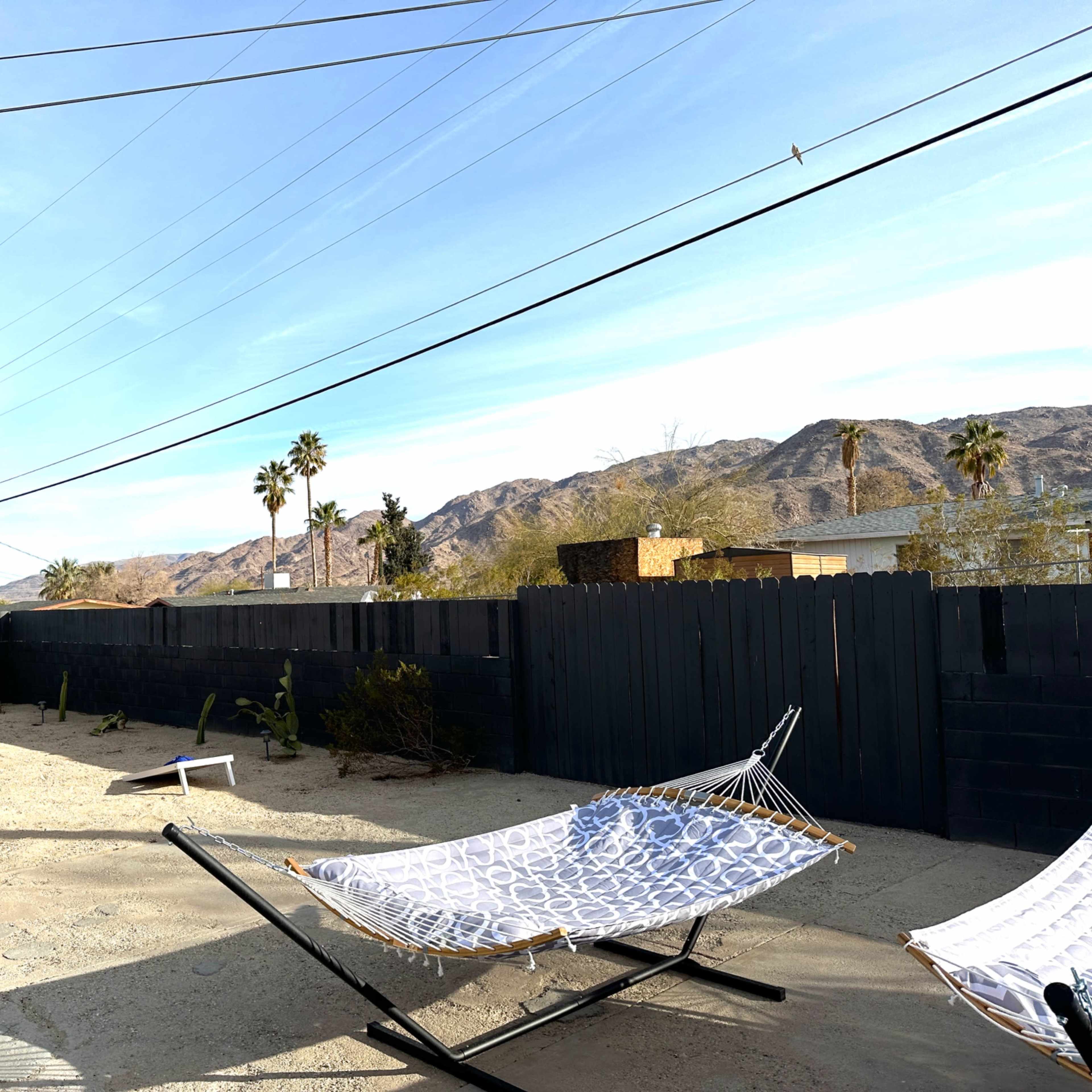 A vacant backyard features two hammocks, desert vegetation, and mountains in the background under a clear sky.