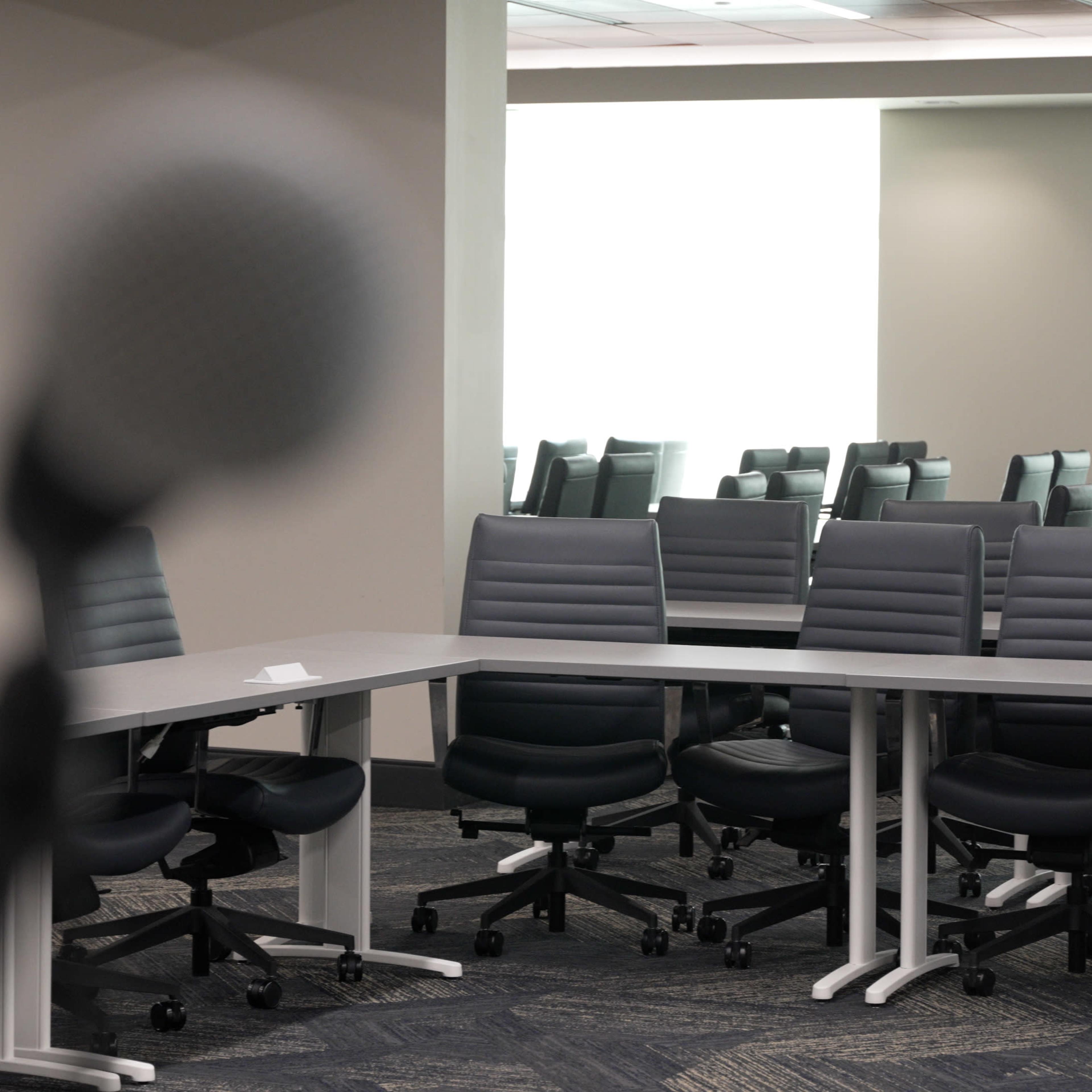 A conference room with a large table and multiple gray office chairs is set up for a meeting.