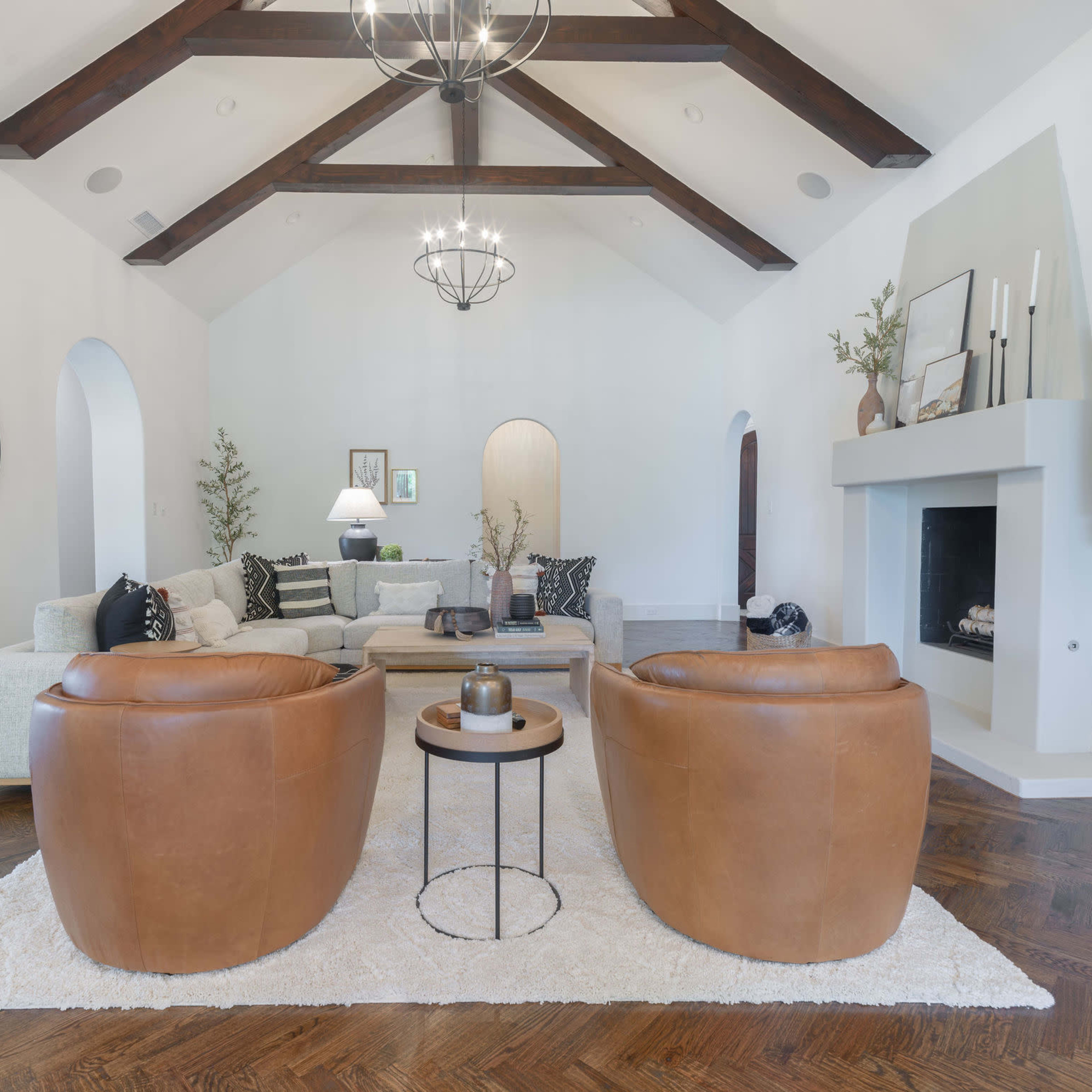 A spacious living room features two brown leather chairs facing a coffee table, with a light-colored sectional sofa and a fireplace in the background.