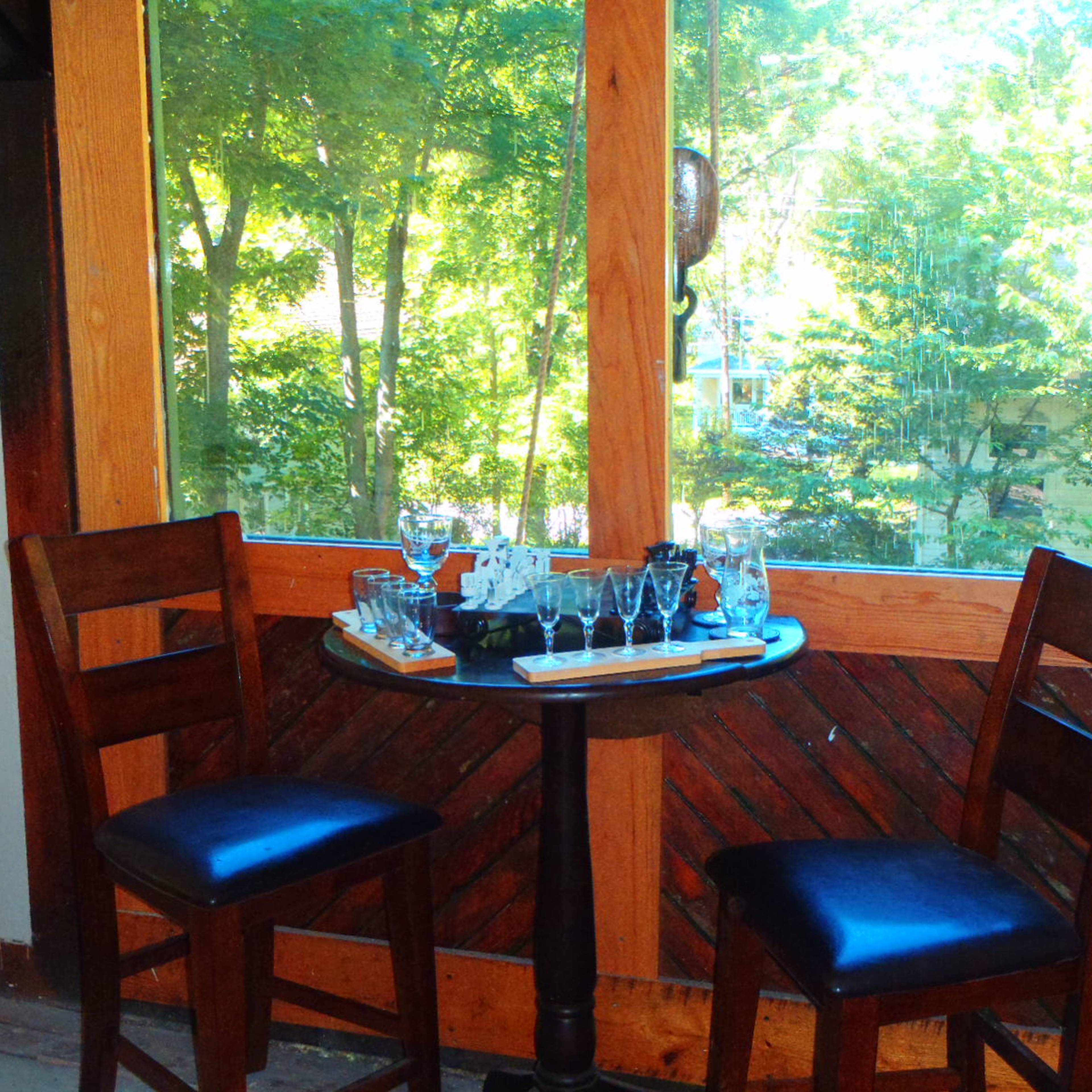 A small table with two wooden chairs is set near a large window overlooking trees.