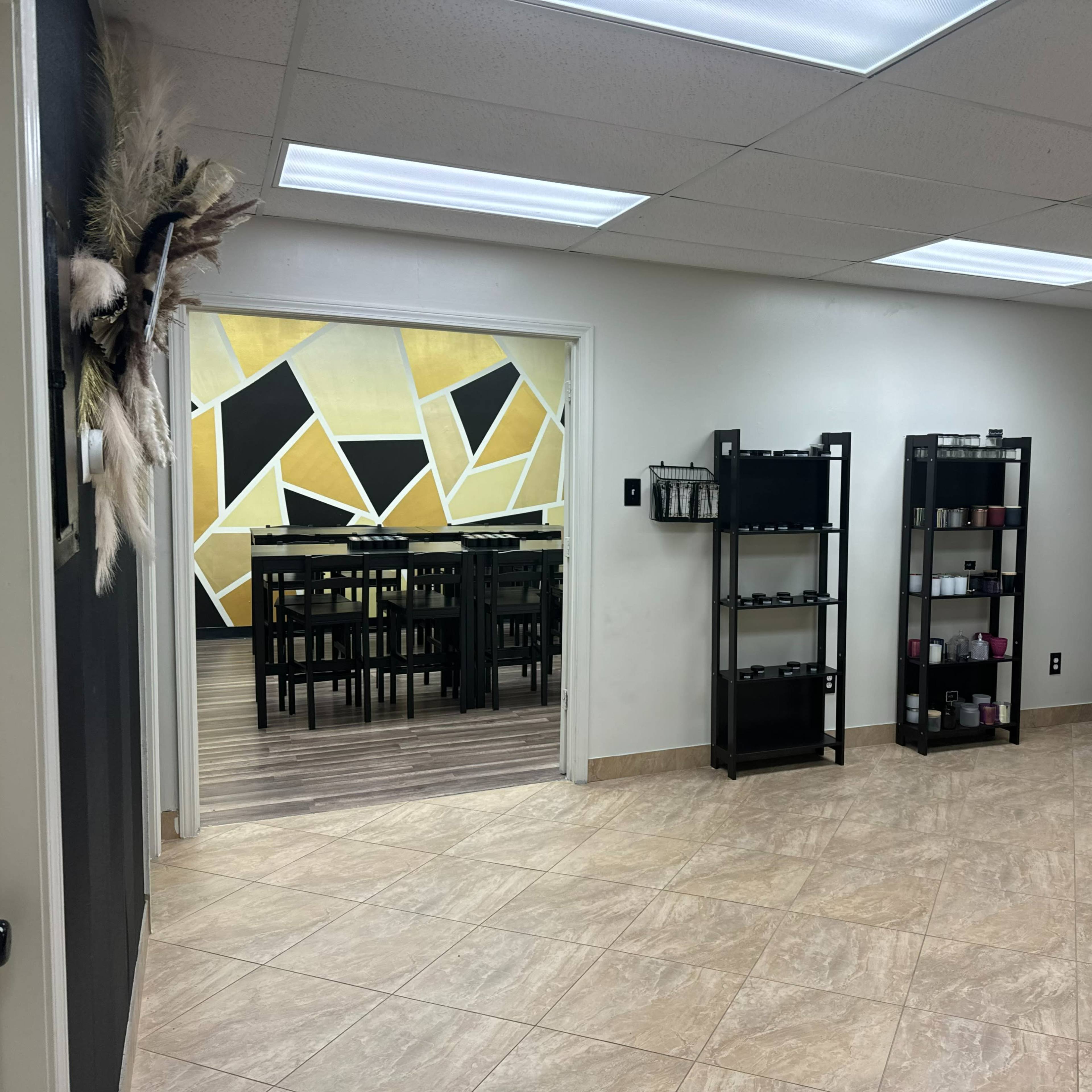 A well-lit room with tile flooring, featuring shelves with products on the right and an adjoining area with a large table and chairs in the background.