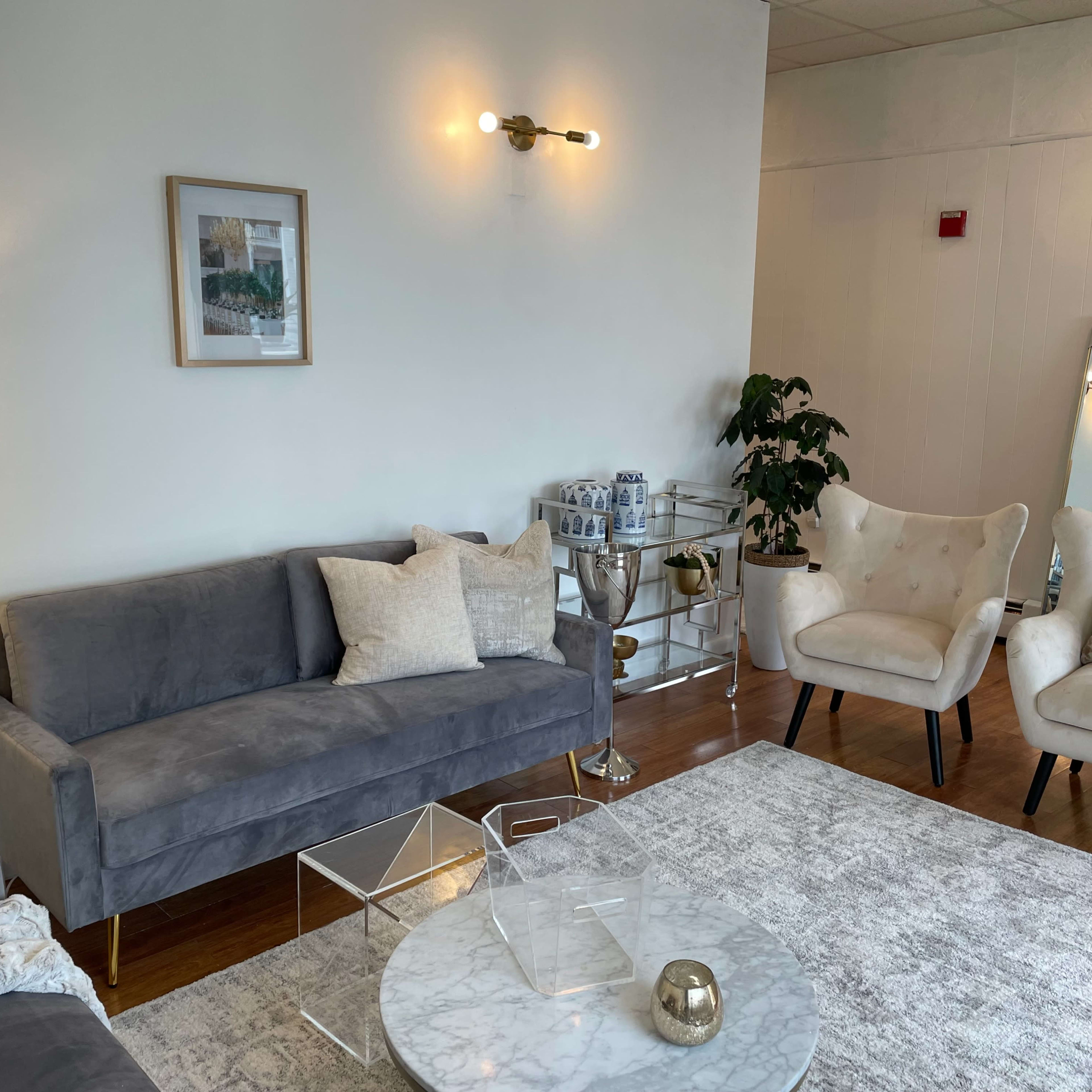 A modern living room features a gray sofa, two white armchairs, a marble coffee table, and a decorative lamp, all arranged on a light area rug.