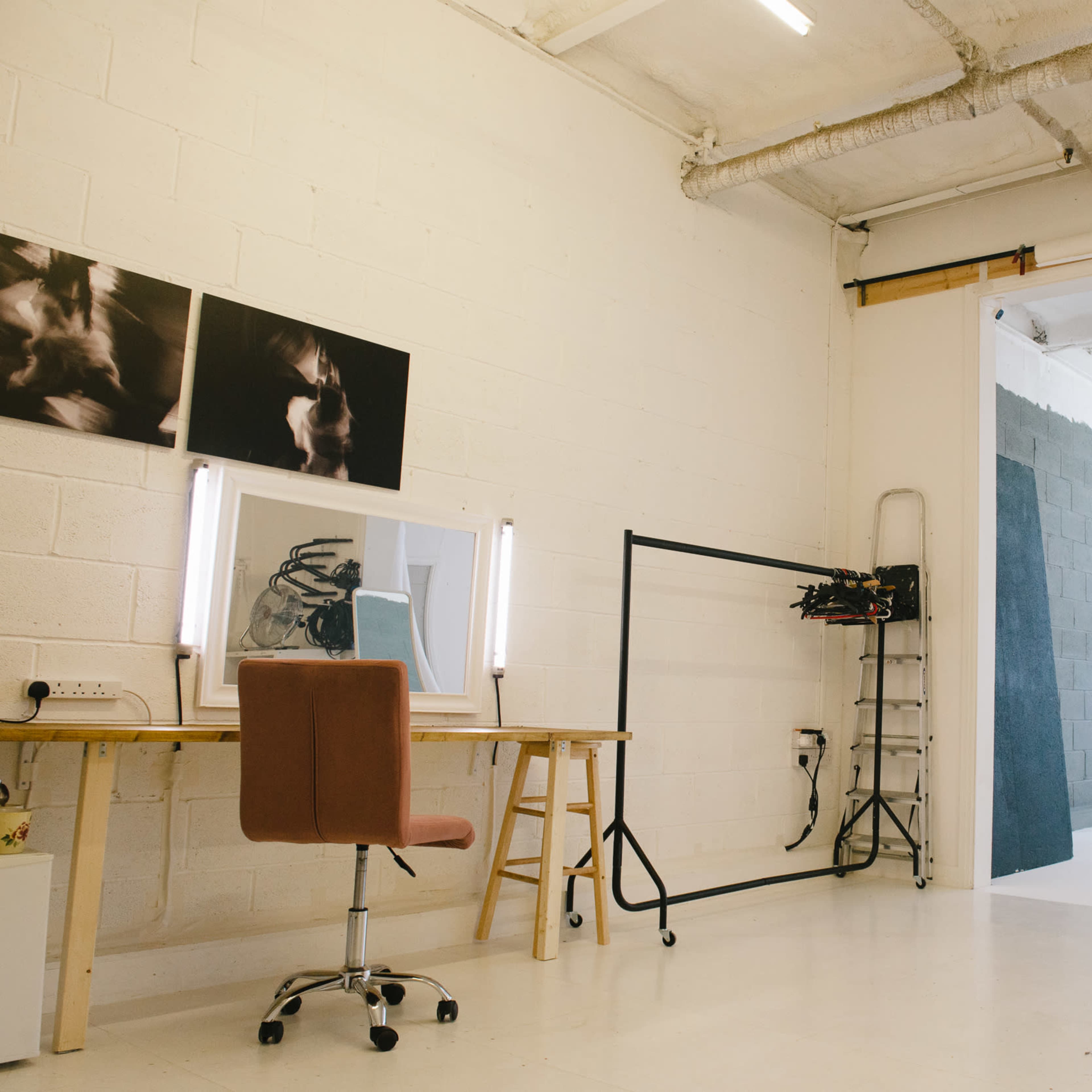 A minimalist studio space with a wooden desk and chair, a large window, and studio lighting equipment.
