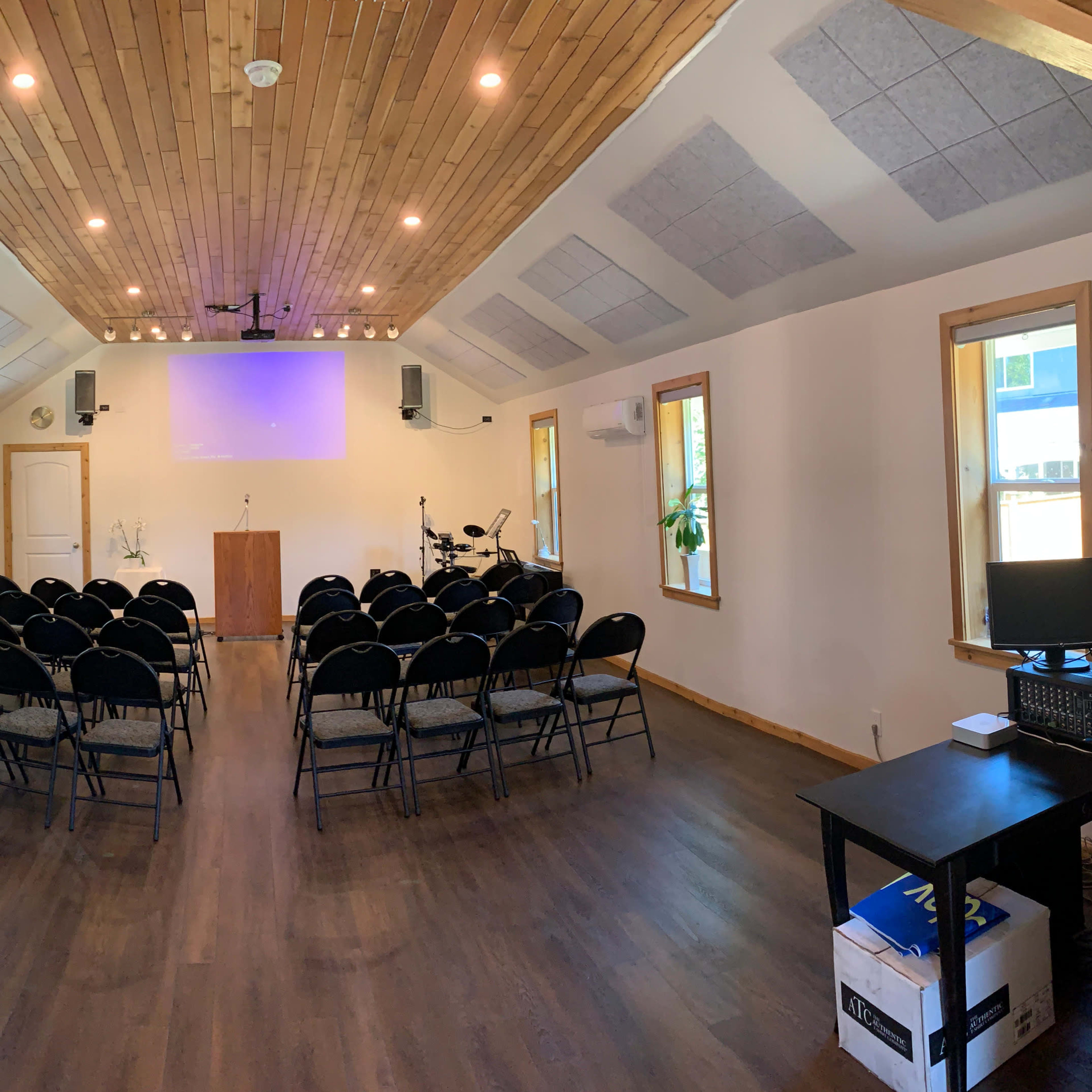 An interior of a small auditorium with rows of black chairs, a podium at the front, and a sound system setup.