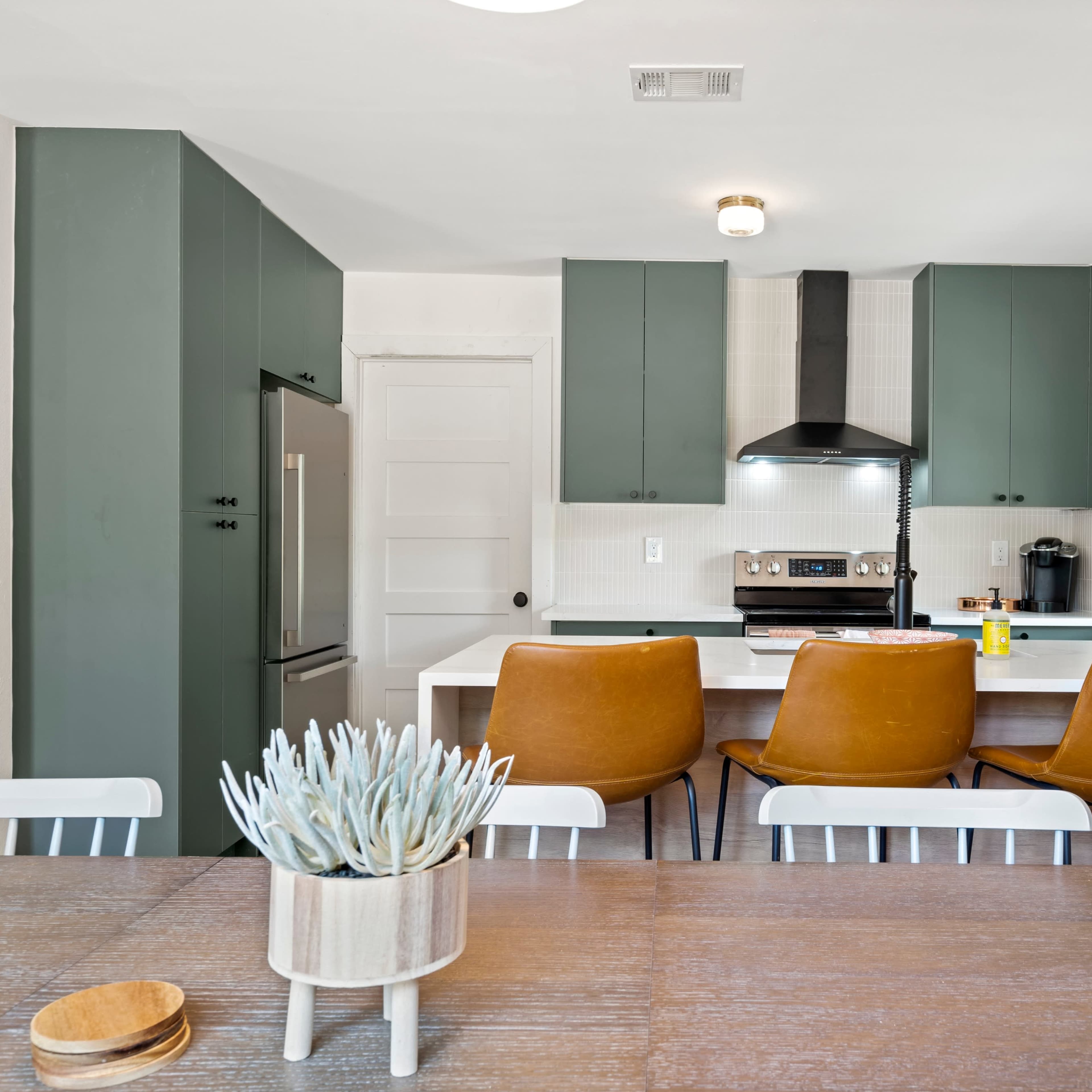 A modern kitchen features green cabinetry, a gray countertop, and a dining table with a small succulent centerpiece.