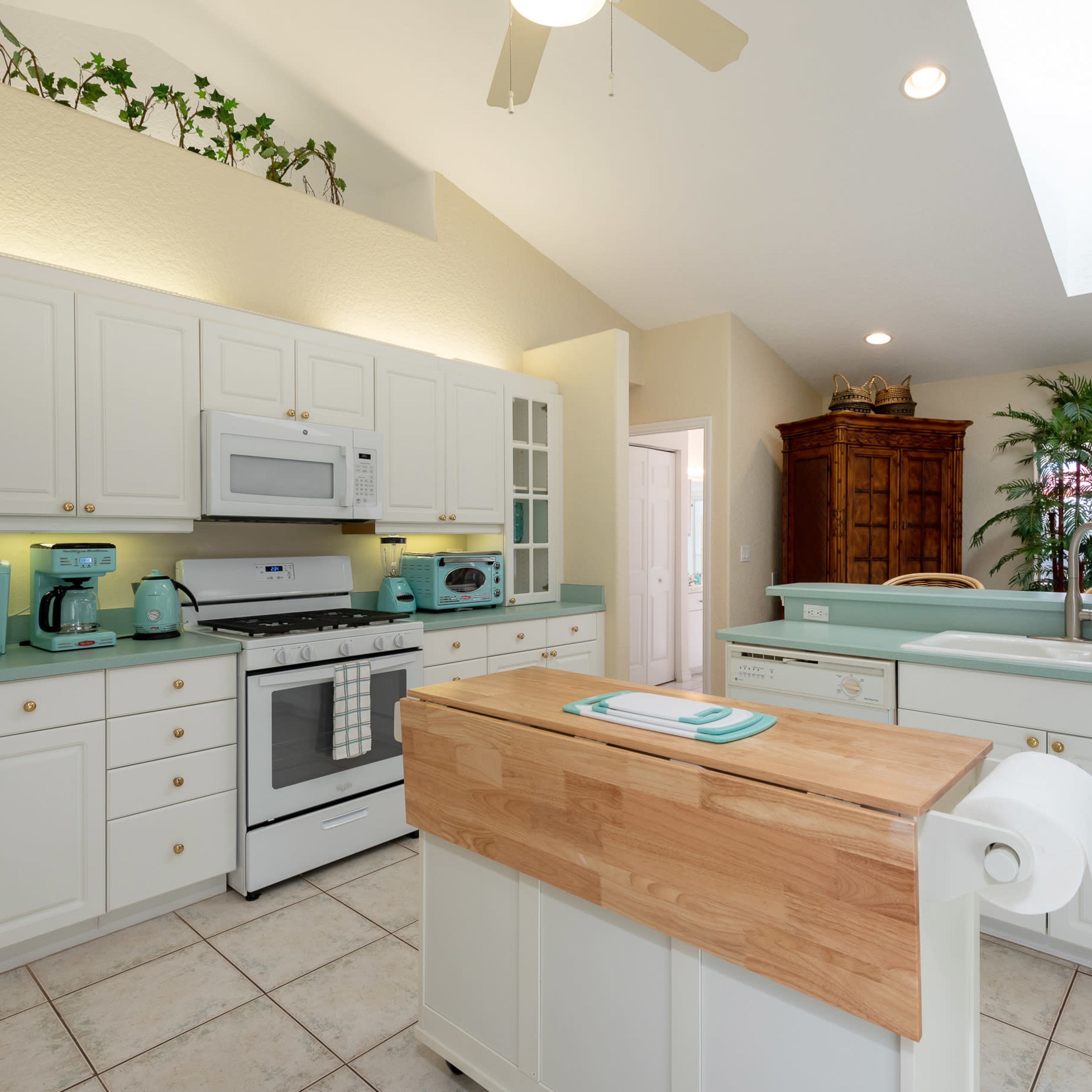 A modern kitchen features white cabinetry, a central wooden island, and light-colored countertops, with appliances in mint green and ample natural light.