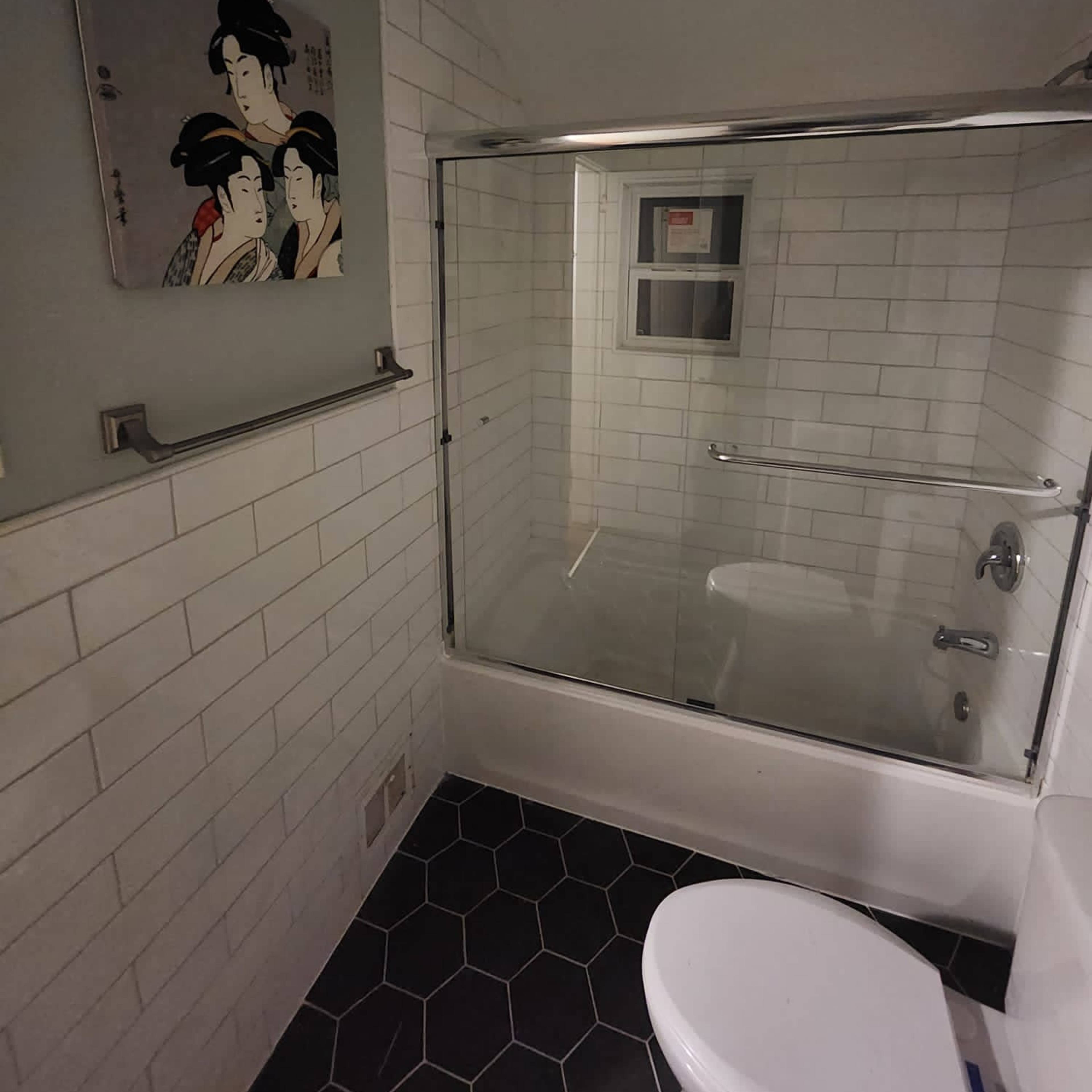 A bathroom with a glass shower enclosure, a toilet, and a wall featuring a framed artwork of two women.