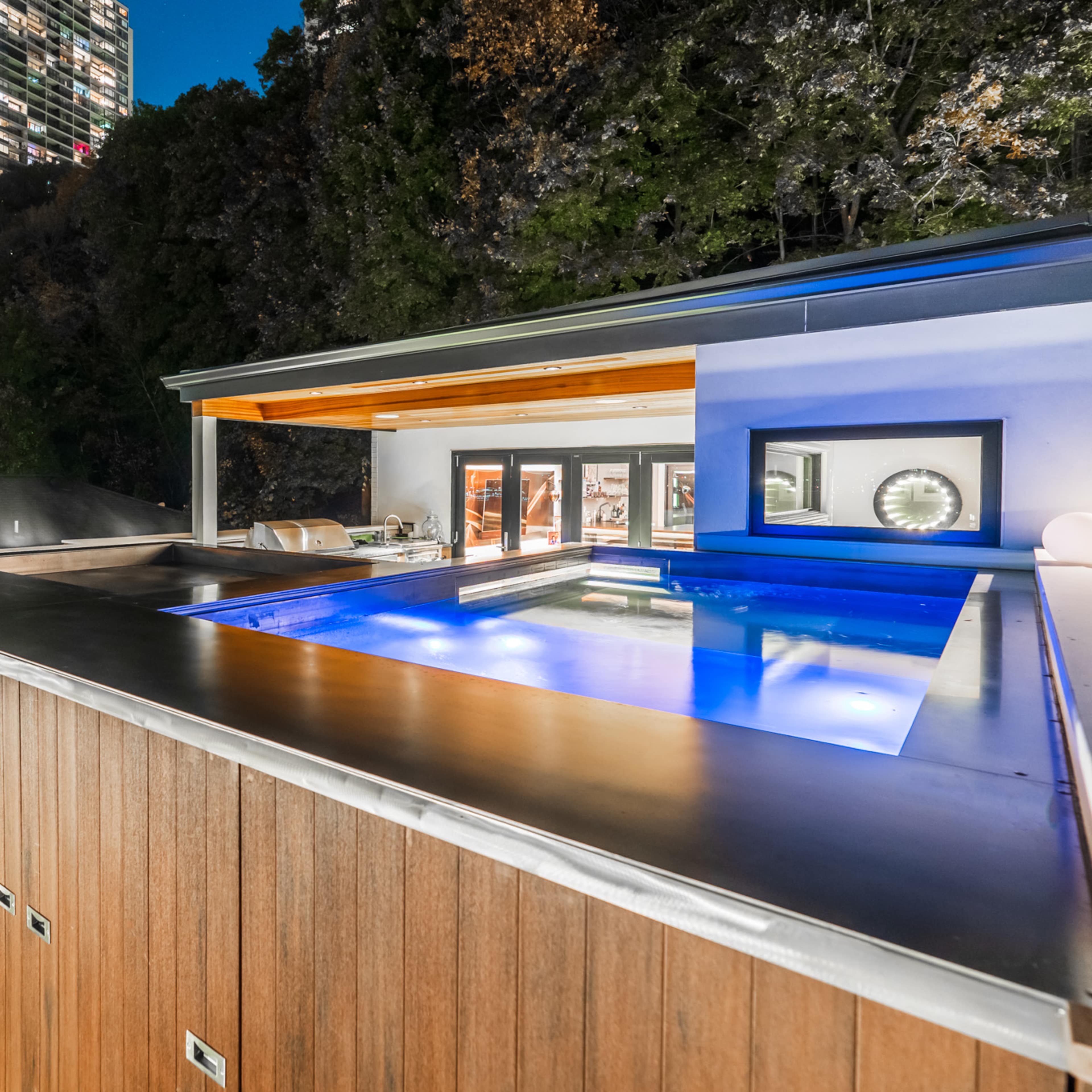 A modern outdoor pool area with a built-in fireplace, overlooking a city skyline at night.