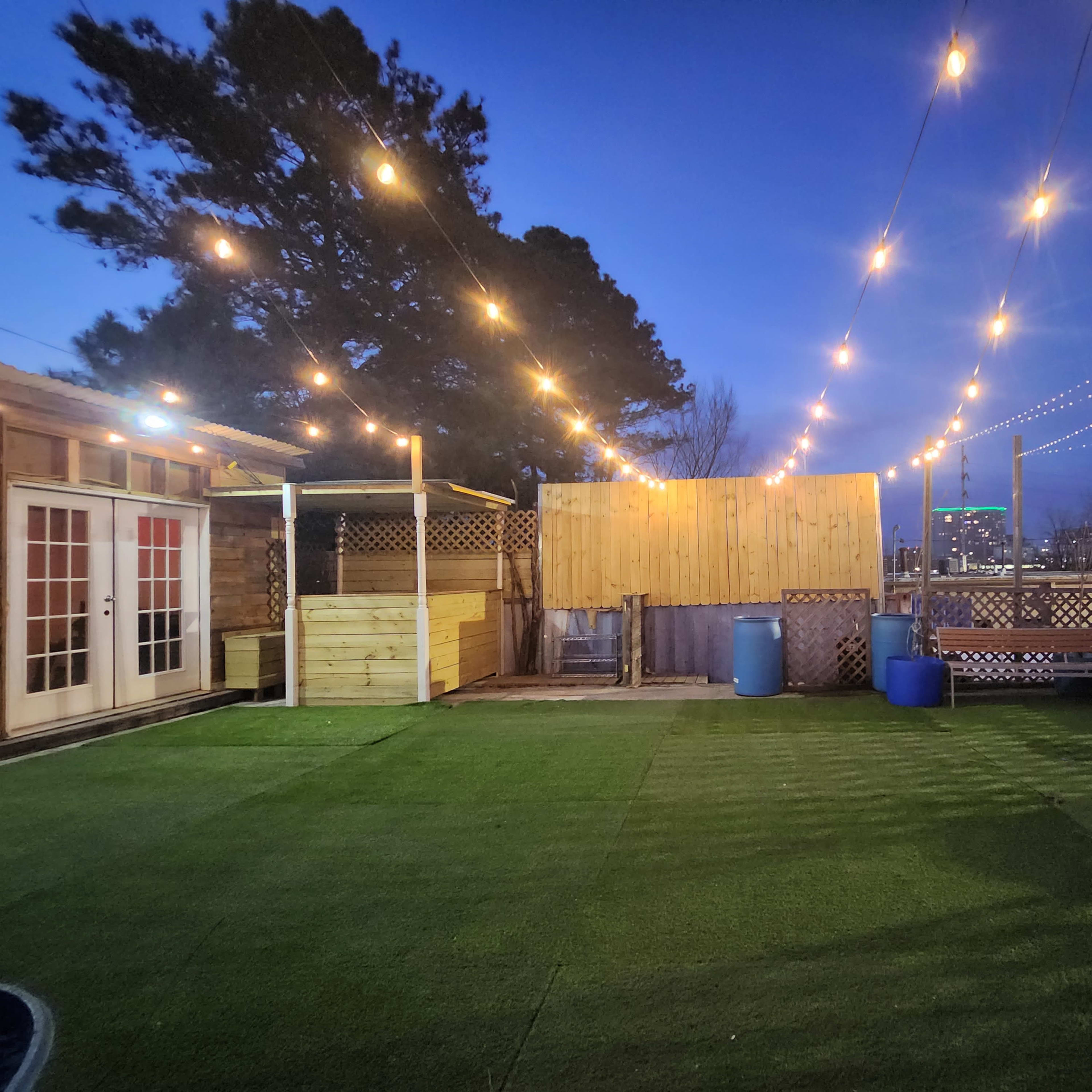 A rooftop patio area illuminated by string lights, featuring artificial grass and wooden structures.