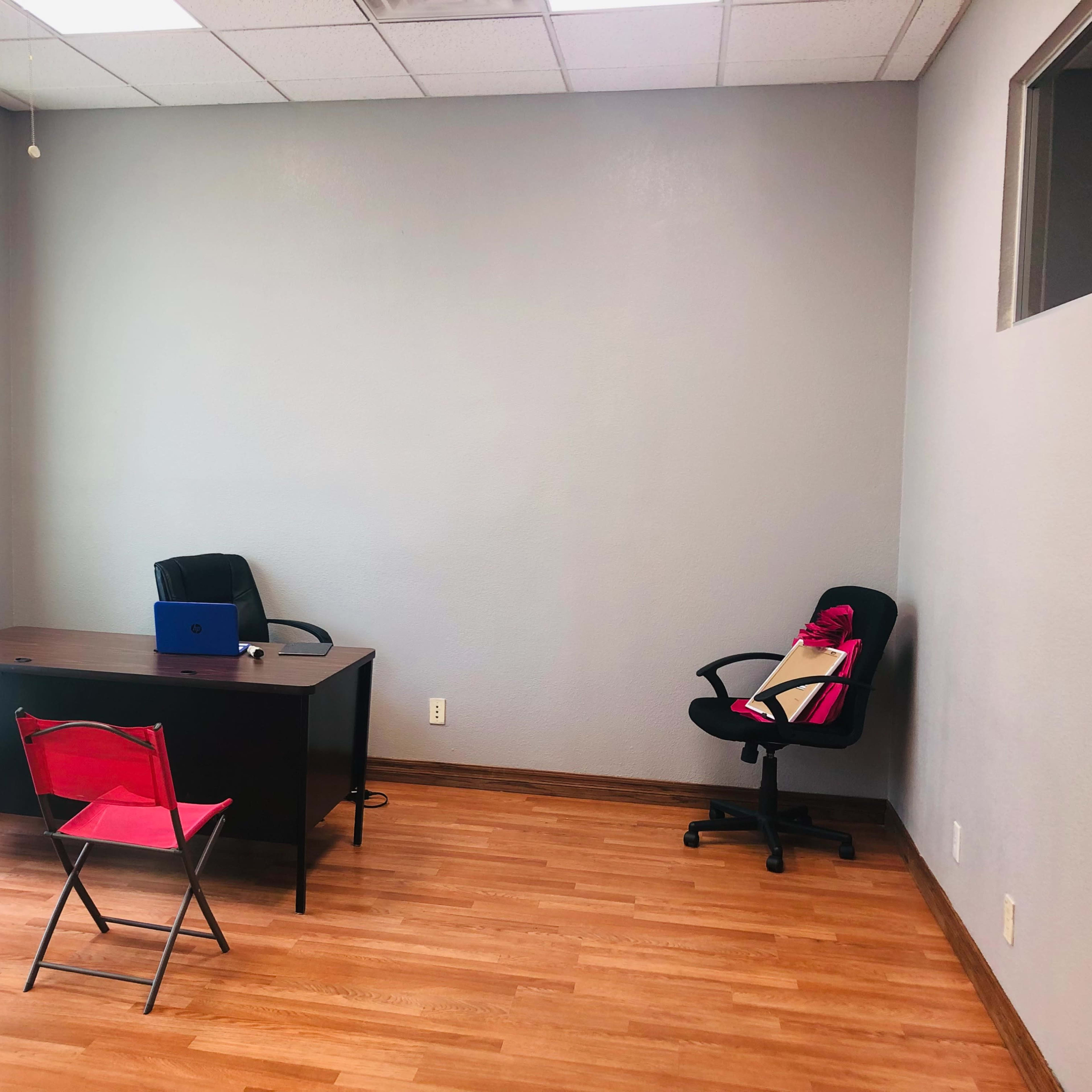 A sparsely furnished office with a desk, two chairs, and a laptop on the desk.