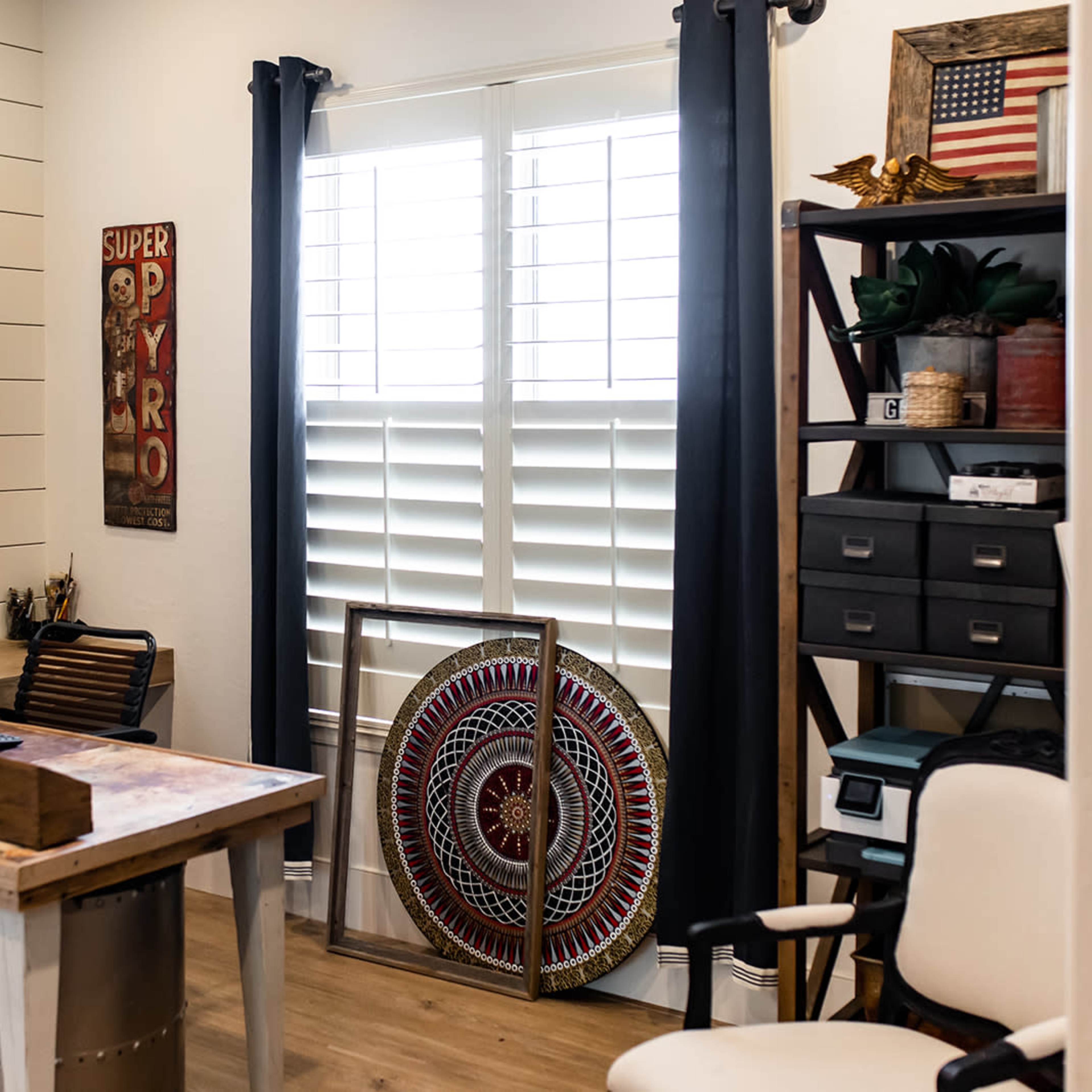 A home office with a desk, a chair, a large decorative shield, and a mirror mounted on the wall.