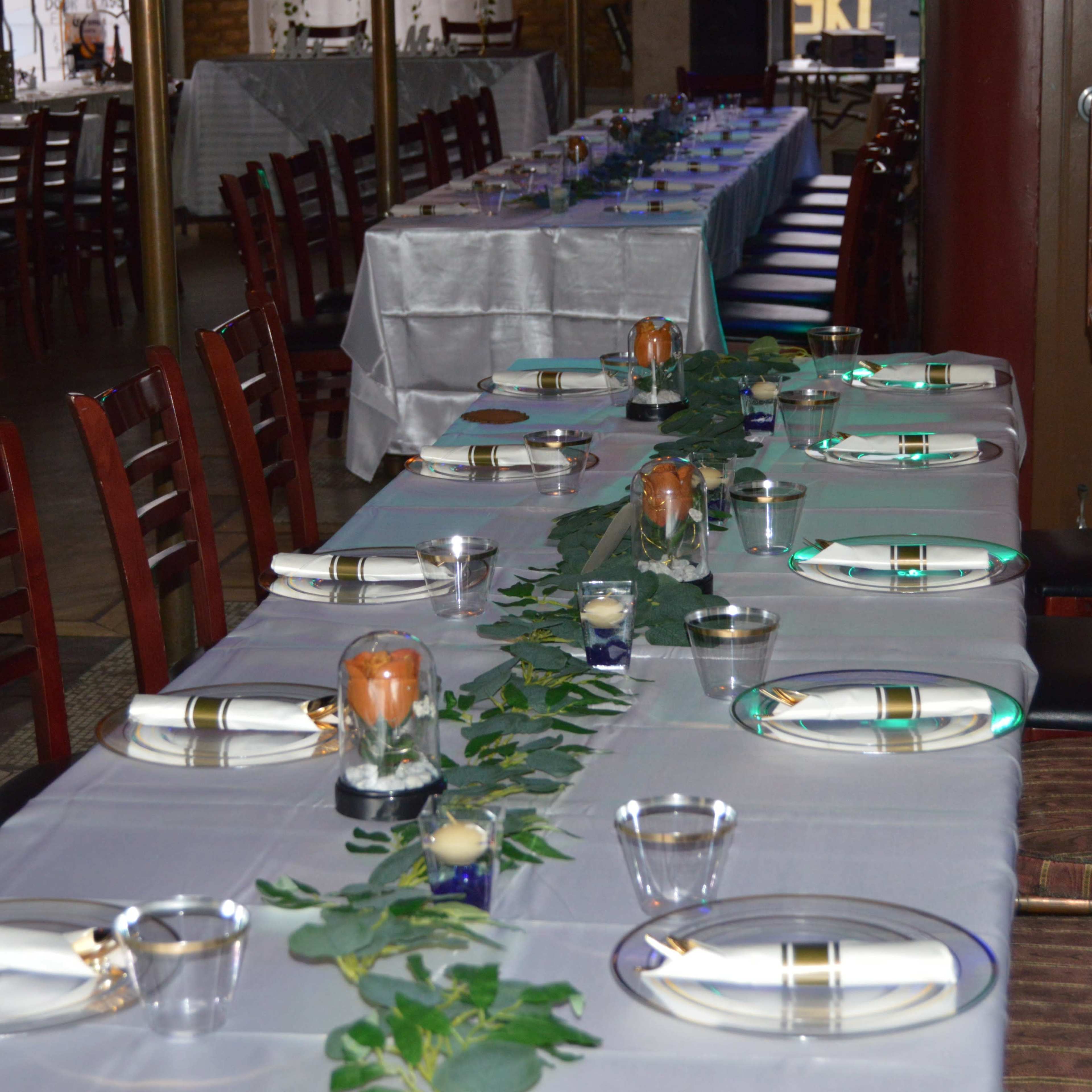 A long dining table is set with plates, utensils, and decorative elements, featuring a green floral runner and candles.